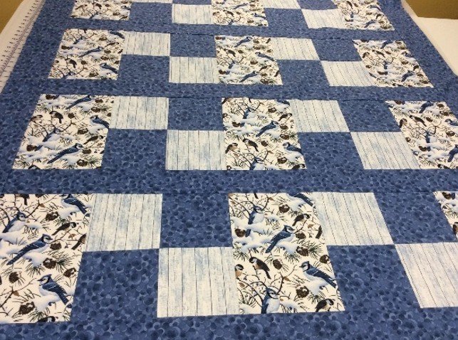 Blue and white patchwork quilt top made with flannel fabrics, showing a beginner-friendly square quilt pattern.