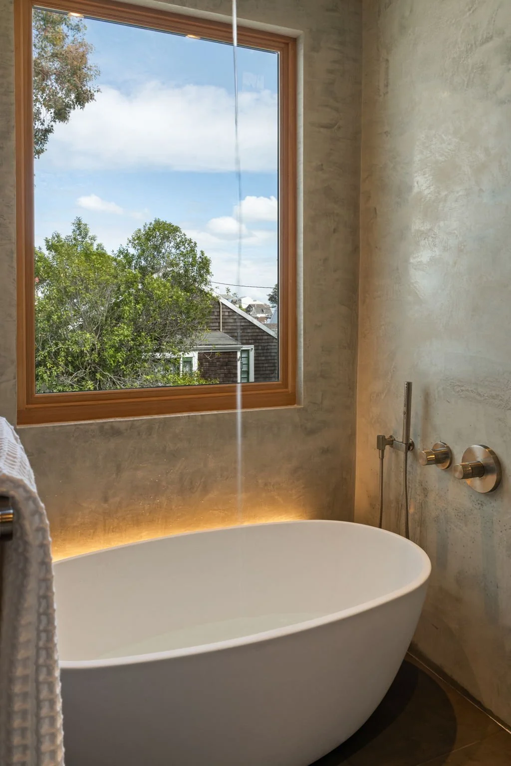 Modern bathroom with a freestanding bathtub, large window with a view of trees and a house, and wall-mounted faucet.