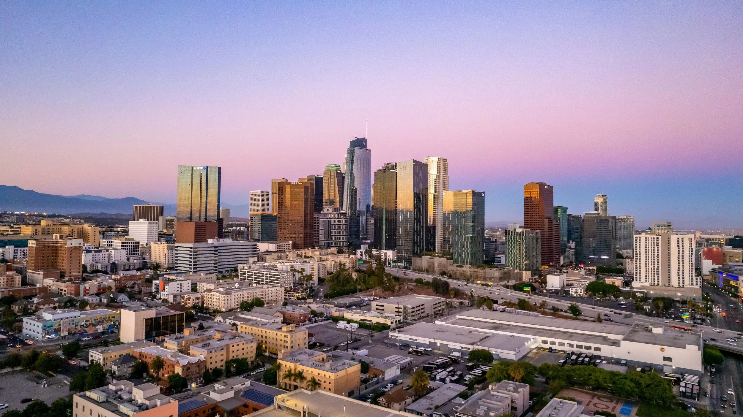City skyline at sunset with tall skyscrapers and colorful sky in Los Angeles.