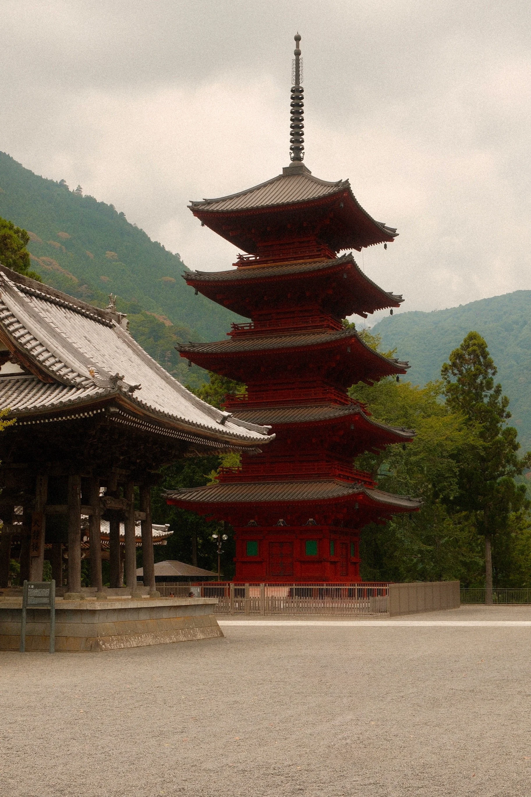 Ein traditioneller japanischer Pagodenturm vor einer bewaldeten Bergkulisse inmitten eines Tempelgeländes.
