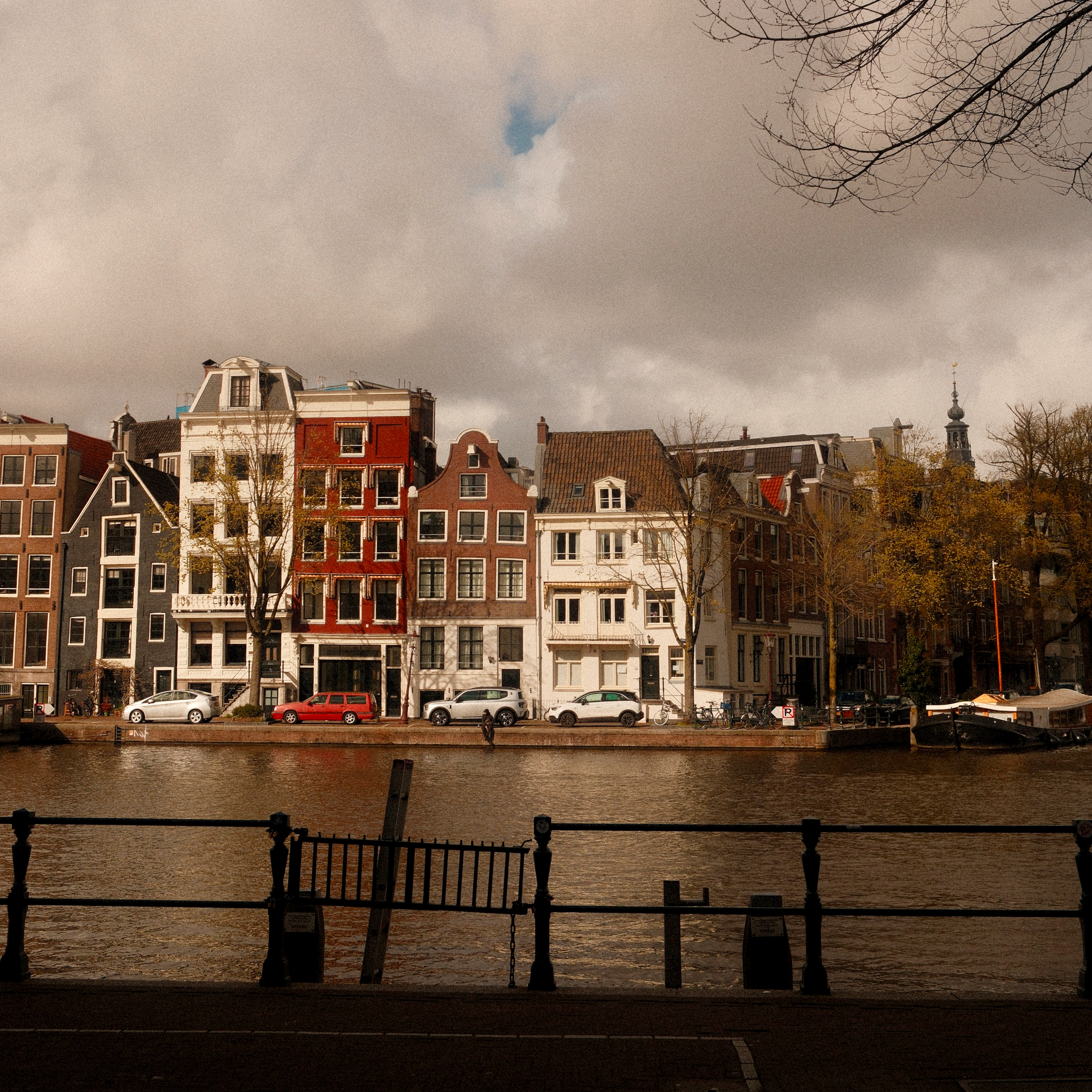 blick aus einem café auf die amstel in amsterdam mit gegenüberliegenden historischen häusern und spiegelndem wasser.