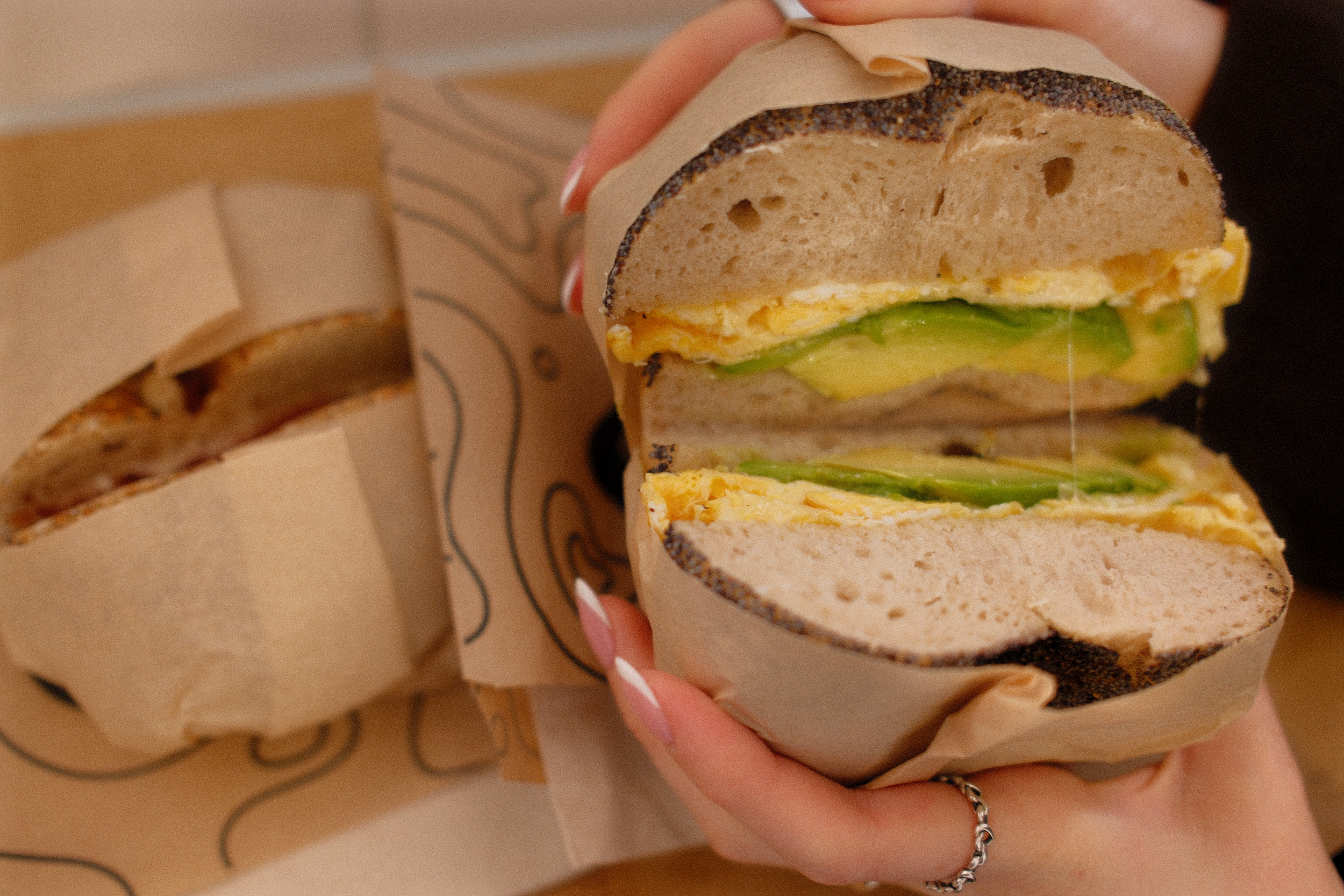 nahaufnahme eines aufgeschnittenen mohnbagels mit avocado und gebratenem ei als frühstück.