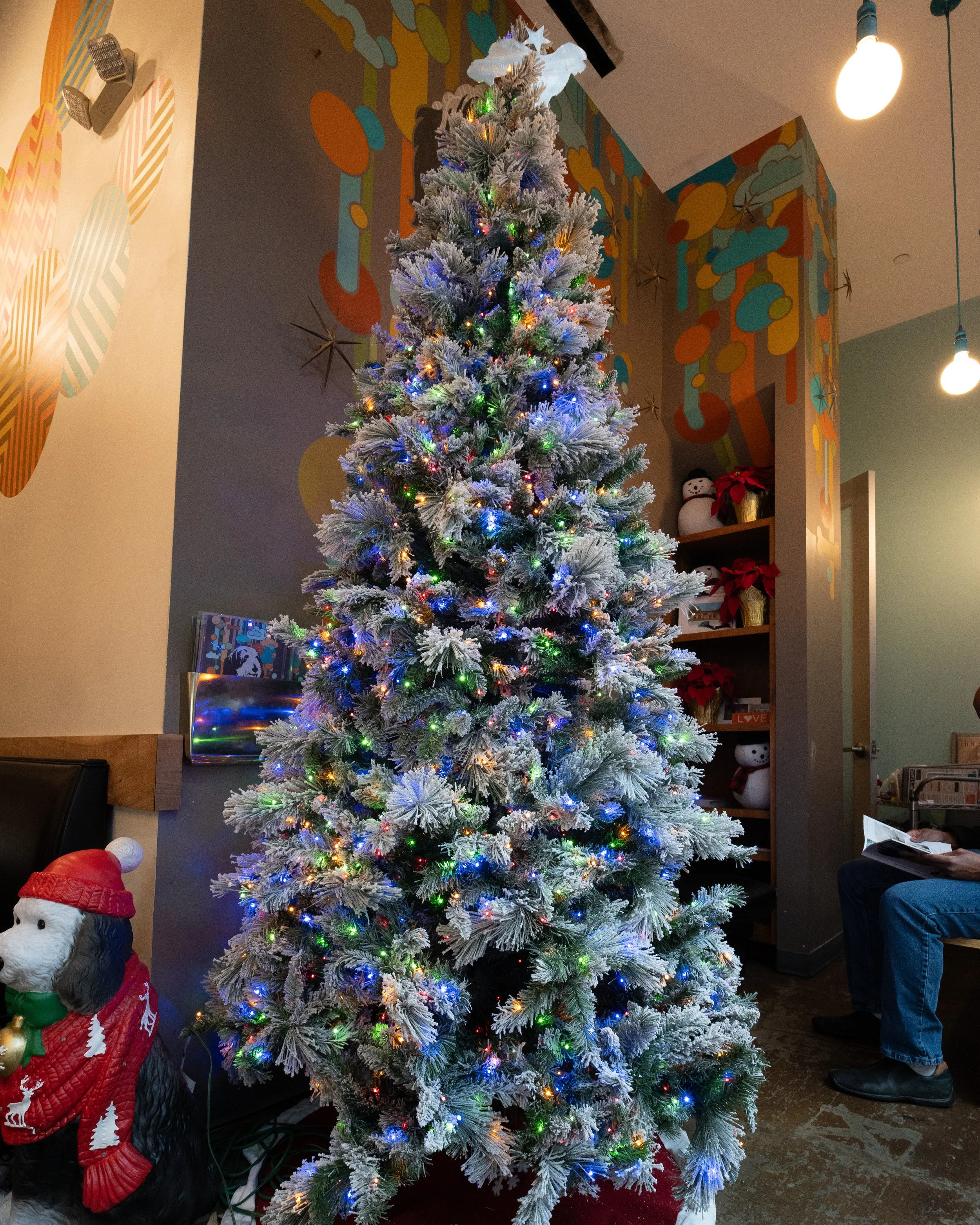 A decorated Christmas tree with multicolored lights and a white star topper in a decorated room with holiday ornaments and wall art.