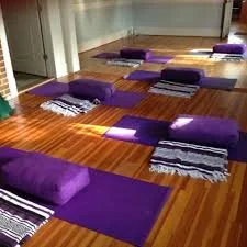 Yoga mats and blankets arranged on a wooden floor in a room.