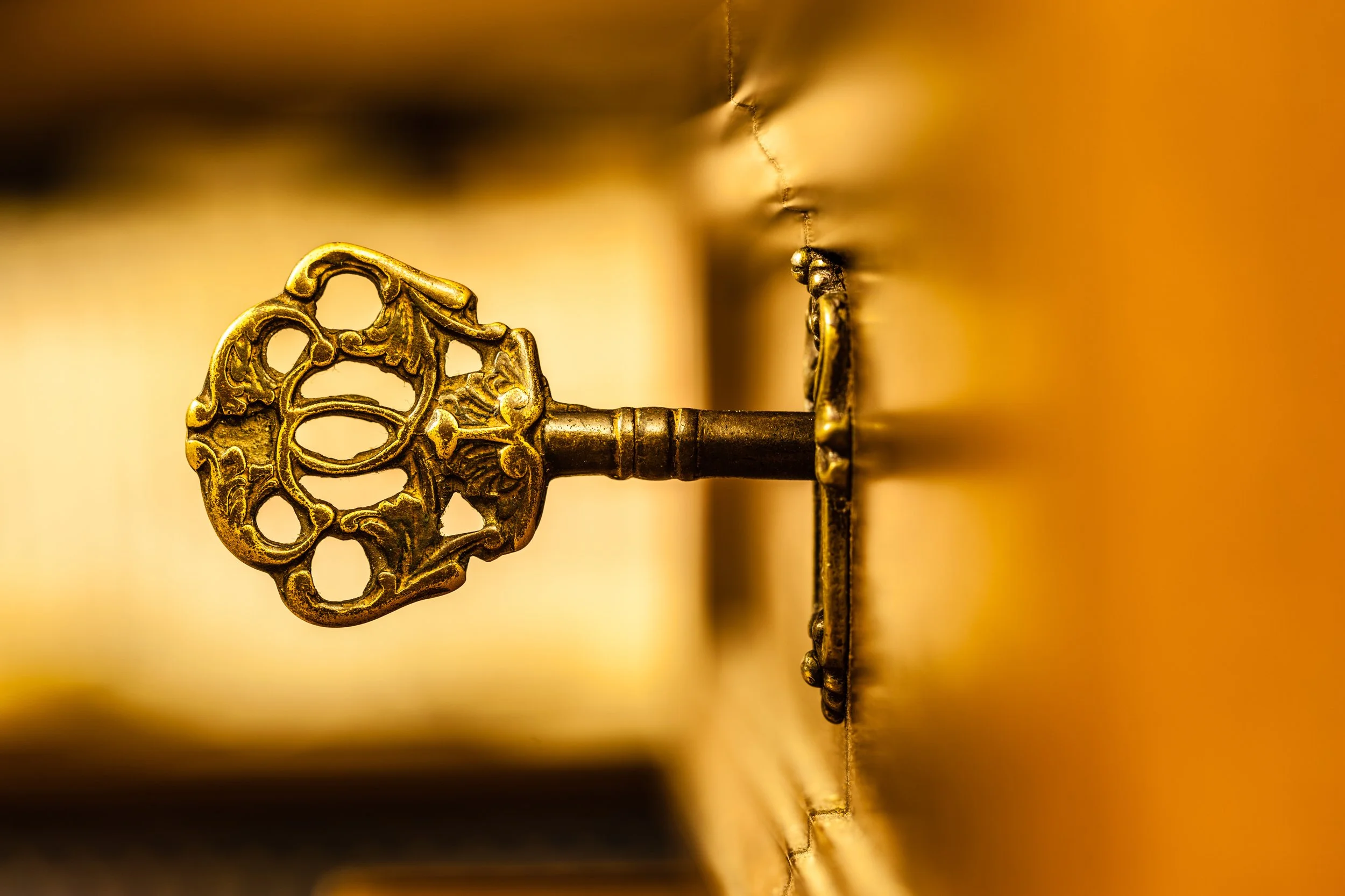 Antique gold key in door with golden glowing background.