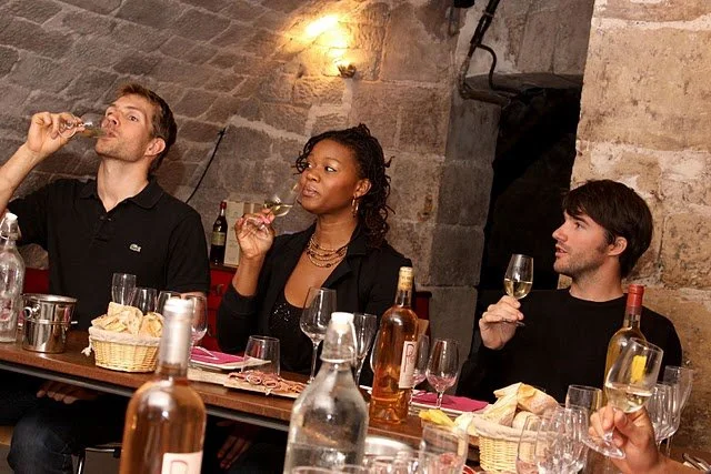 A diverse group of people enjoying wine at a rustic table, highlighting community, culture, and modern wine experiences.