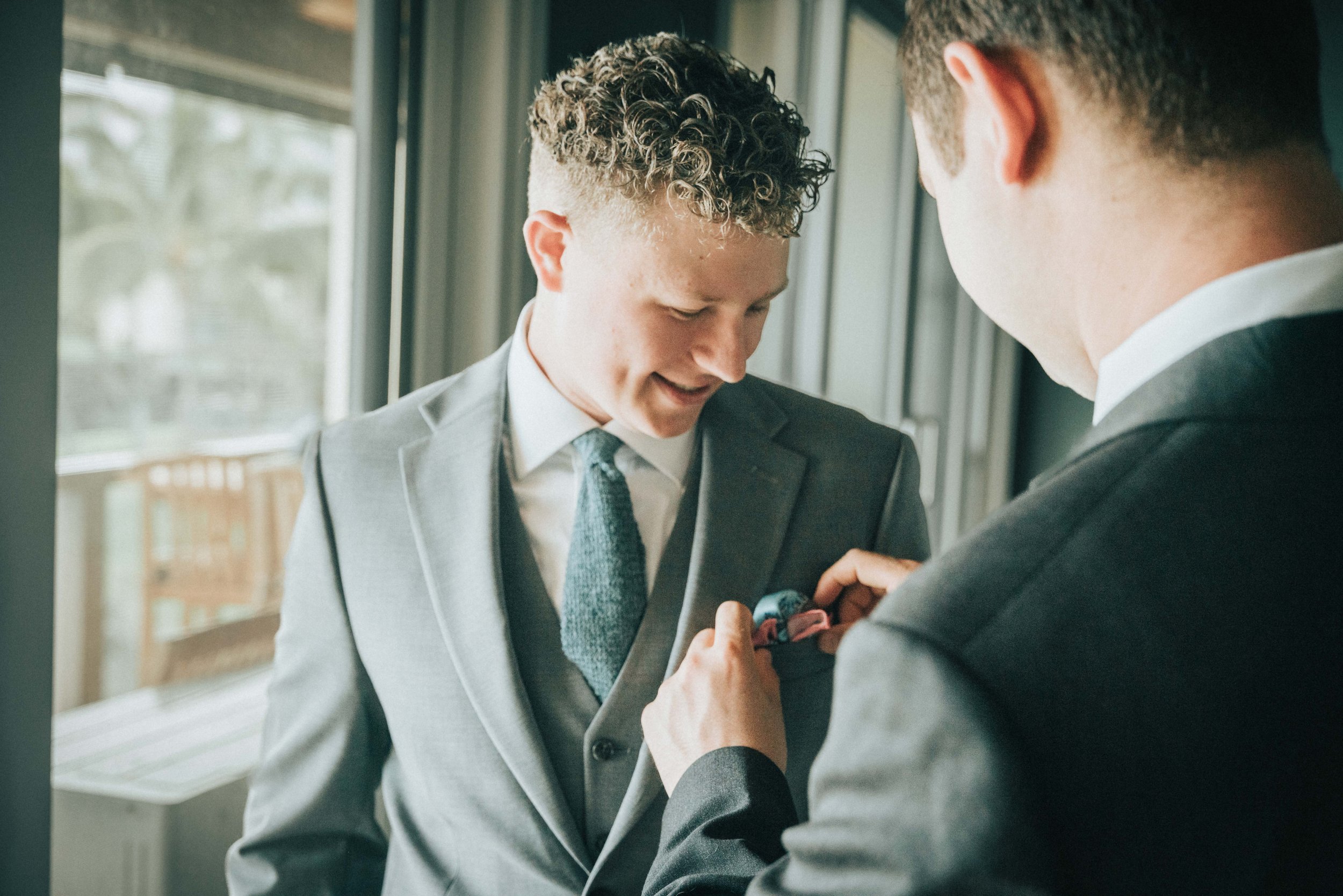 Two men in suits, one adjusting the other's boutonniere