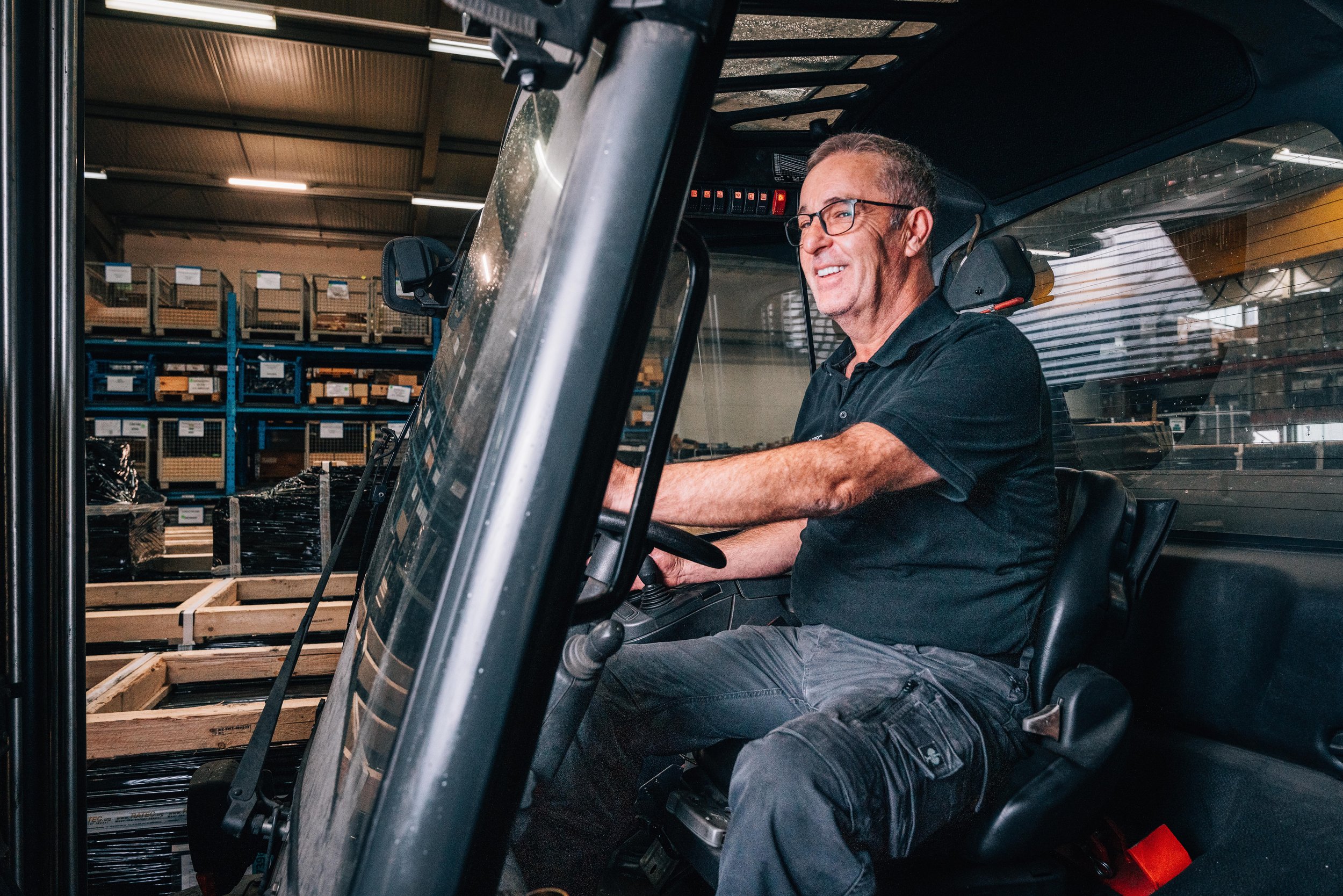 Man driving a forklift in a warehouse with shelves of materials.