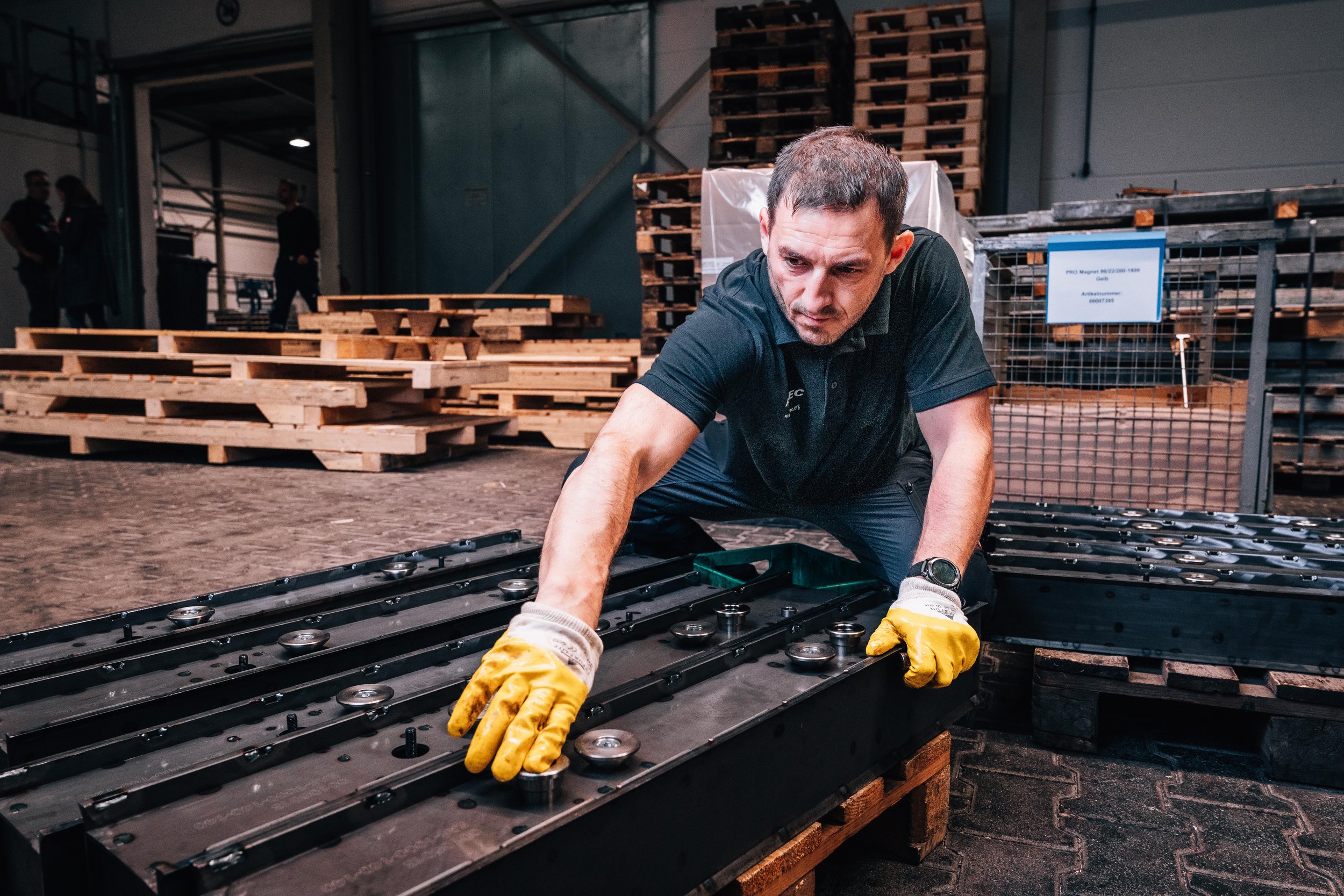 Man wearing yellow gloves inspecting metal machinery parts in industrial setting
