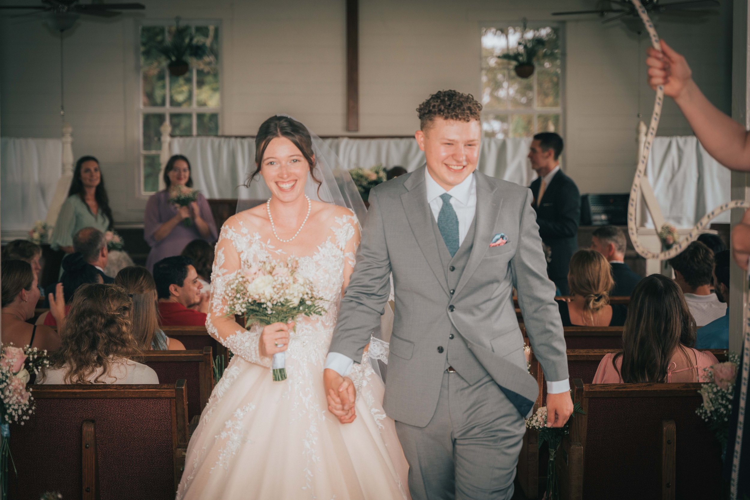 Bride and groom walking down the aisle smiling in a church setting, surrounded by guests.