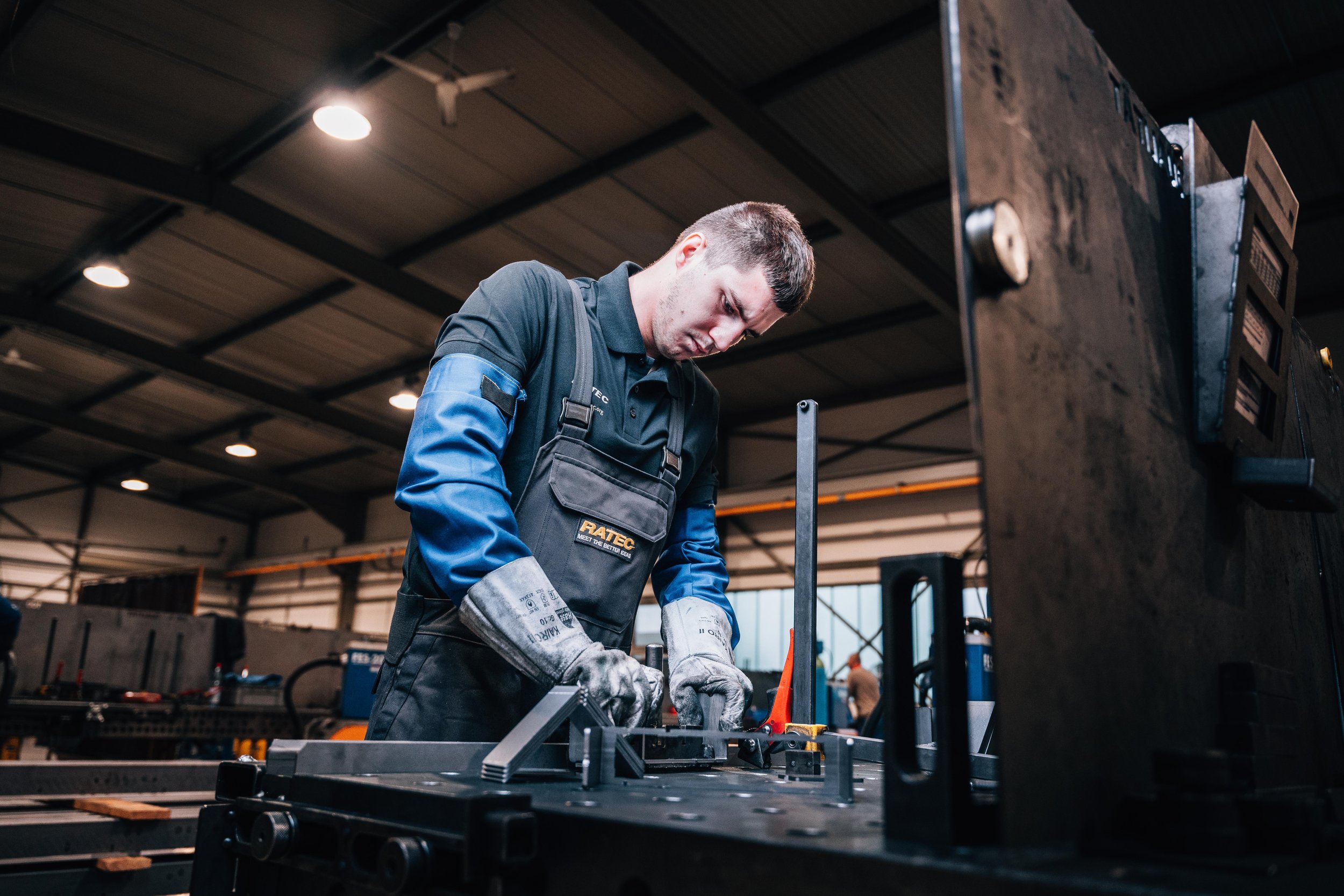 Man in workshop wearing protective gloves and apron working with machinery.