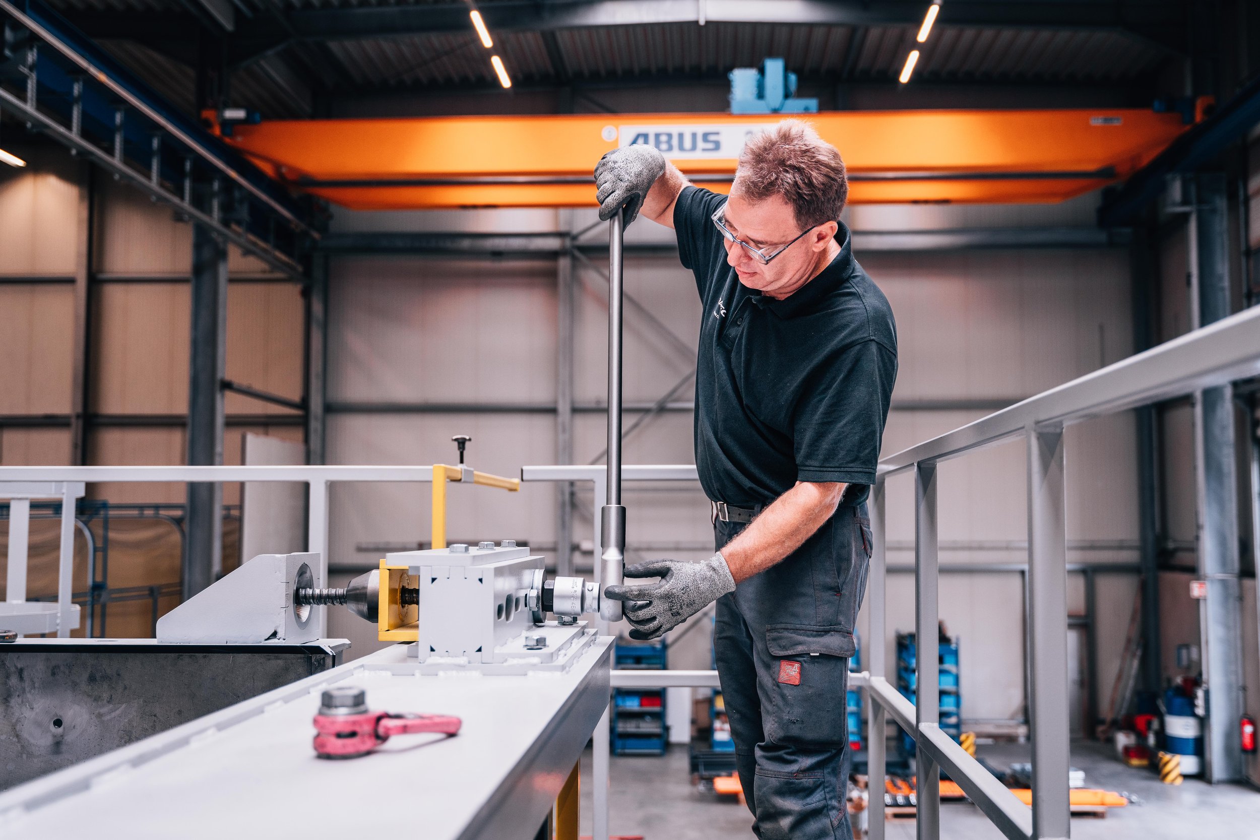 Worker assembling machinery in industrial setting with tools and safety gear.