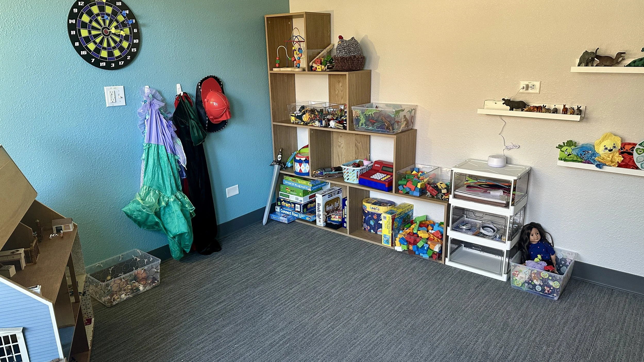 Kids' playroom with toys, shelves, and a dartboard on a blue wall.