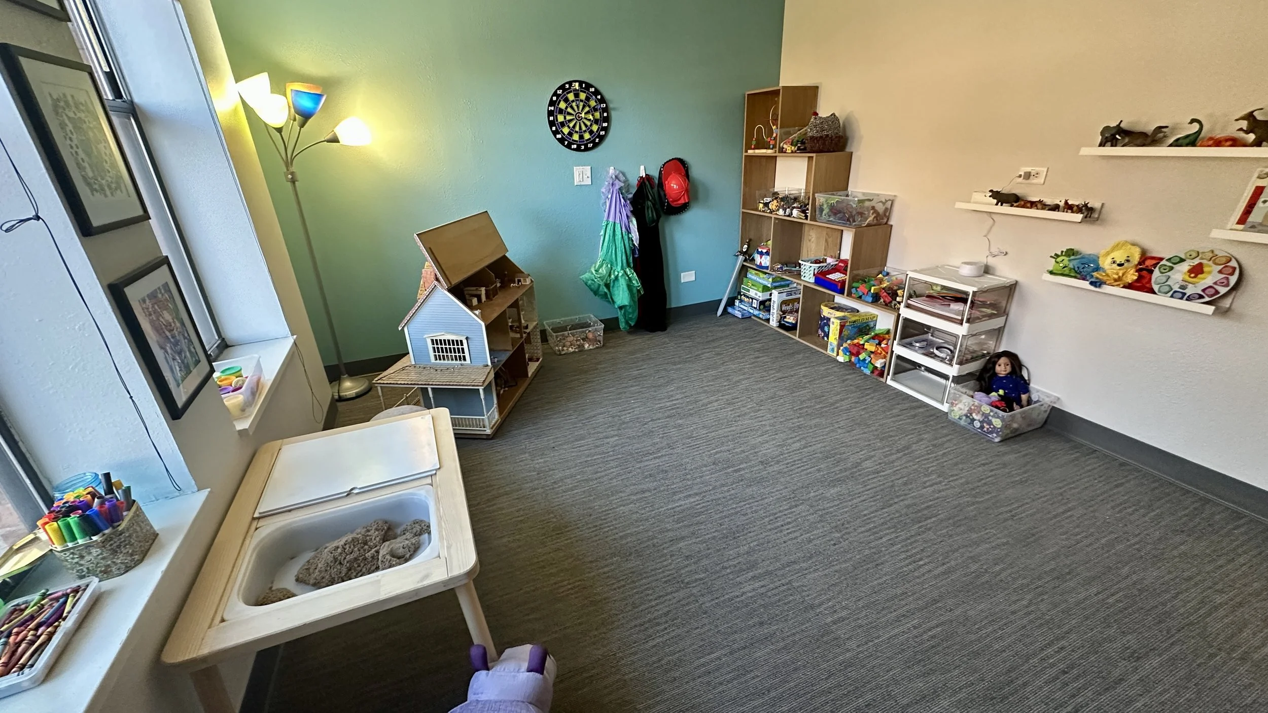 A playroom with toys, shelves, and a dartboard on a blue wall.