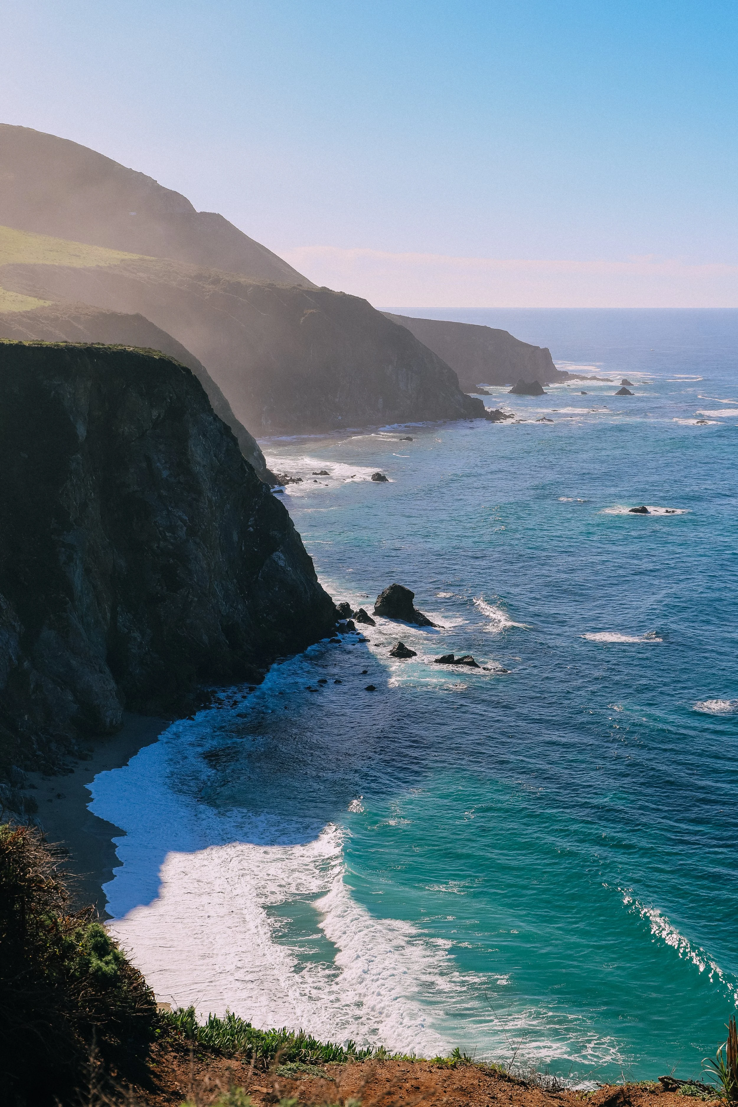 Coastal cliffs with greenery and ocean waves crashing against rocks.