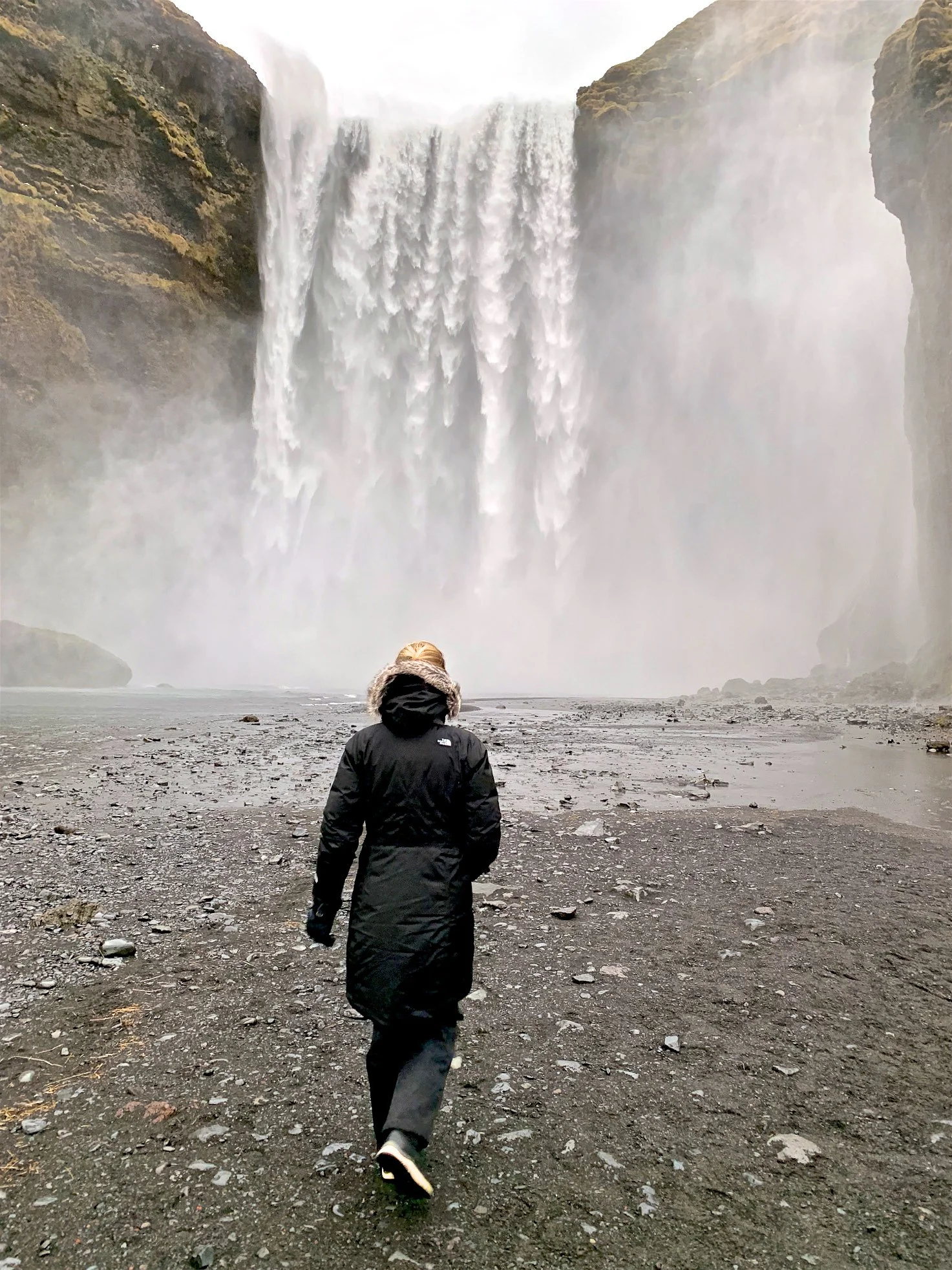 Girl walking towards Skogafoss waterfall in Iceland.