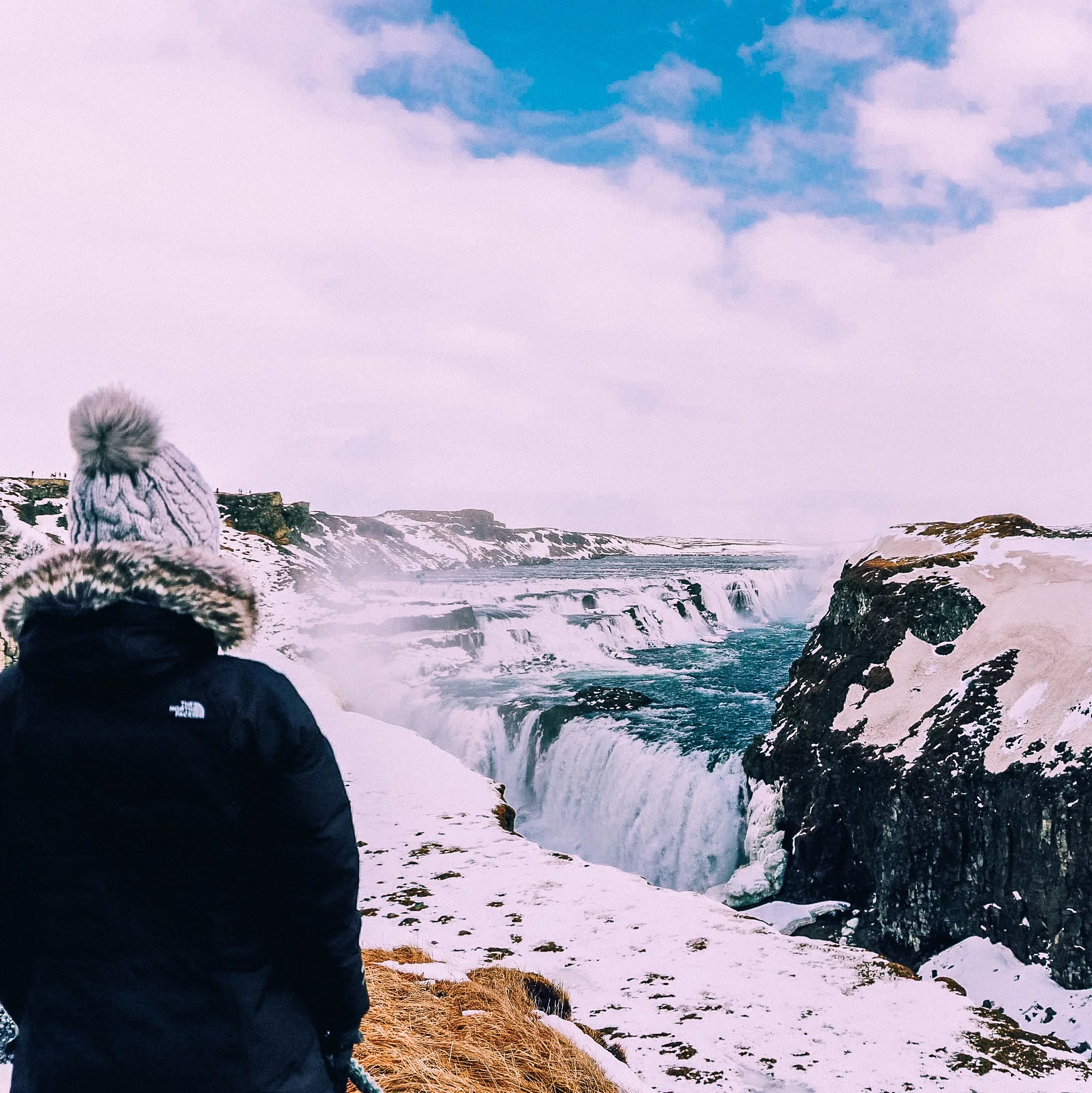 A girl with her back facing the camera and looking towards Gulfoss Waterfall in Iceland.