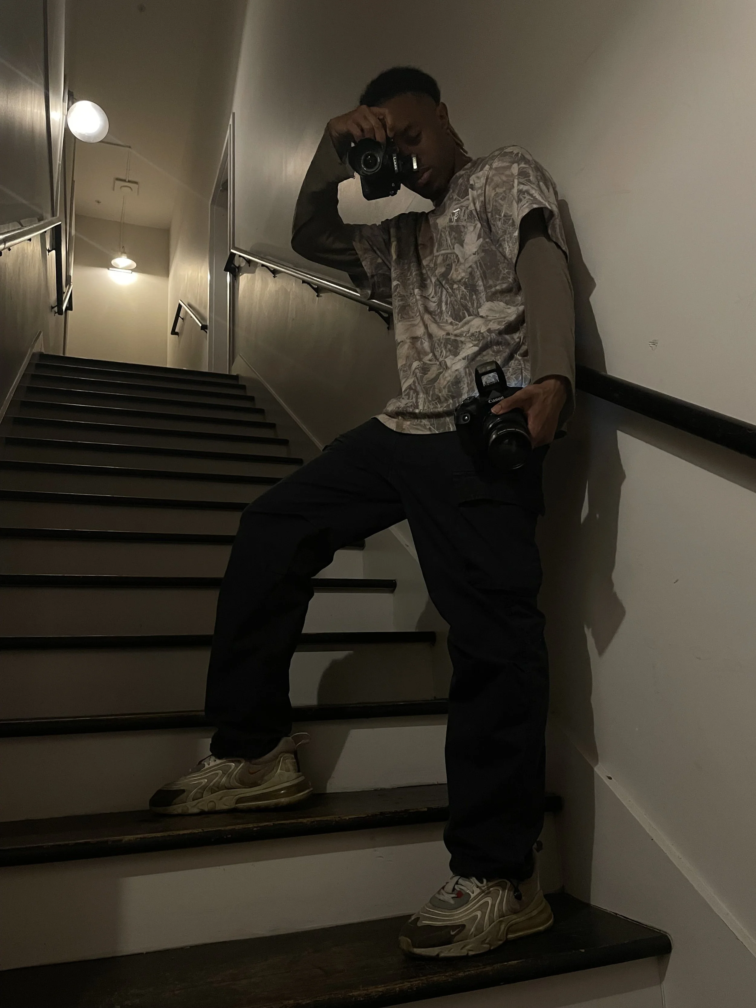 Person holding two cameras on a stairway, wearing casual clothing and sneakers.