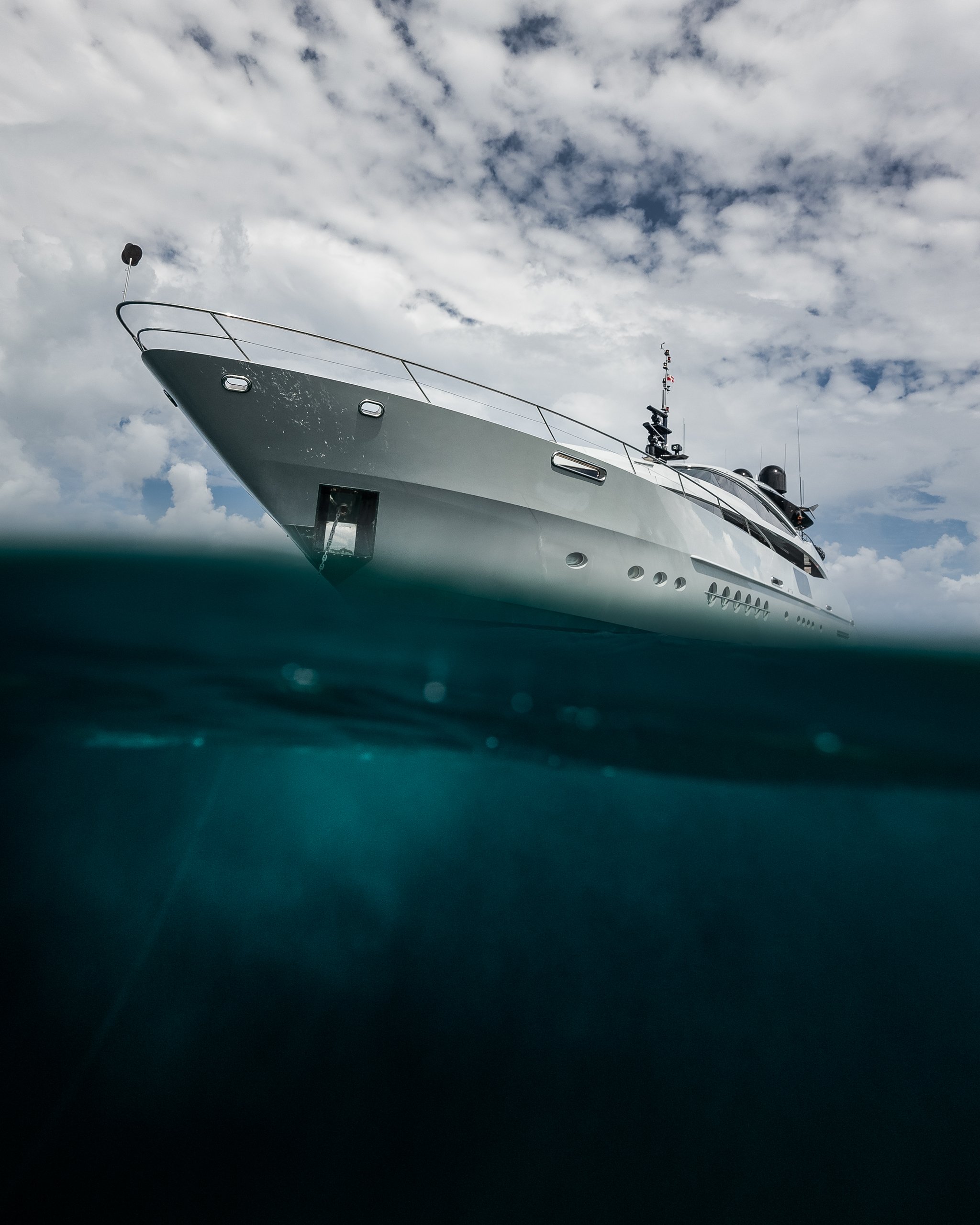 A large white yacht seen from a low angle with part of the water surface visible in the foreground, under a cloudy sky.