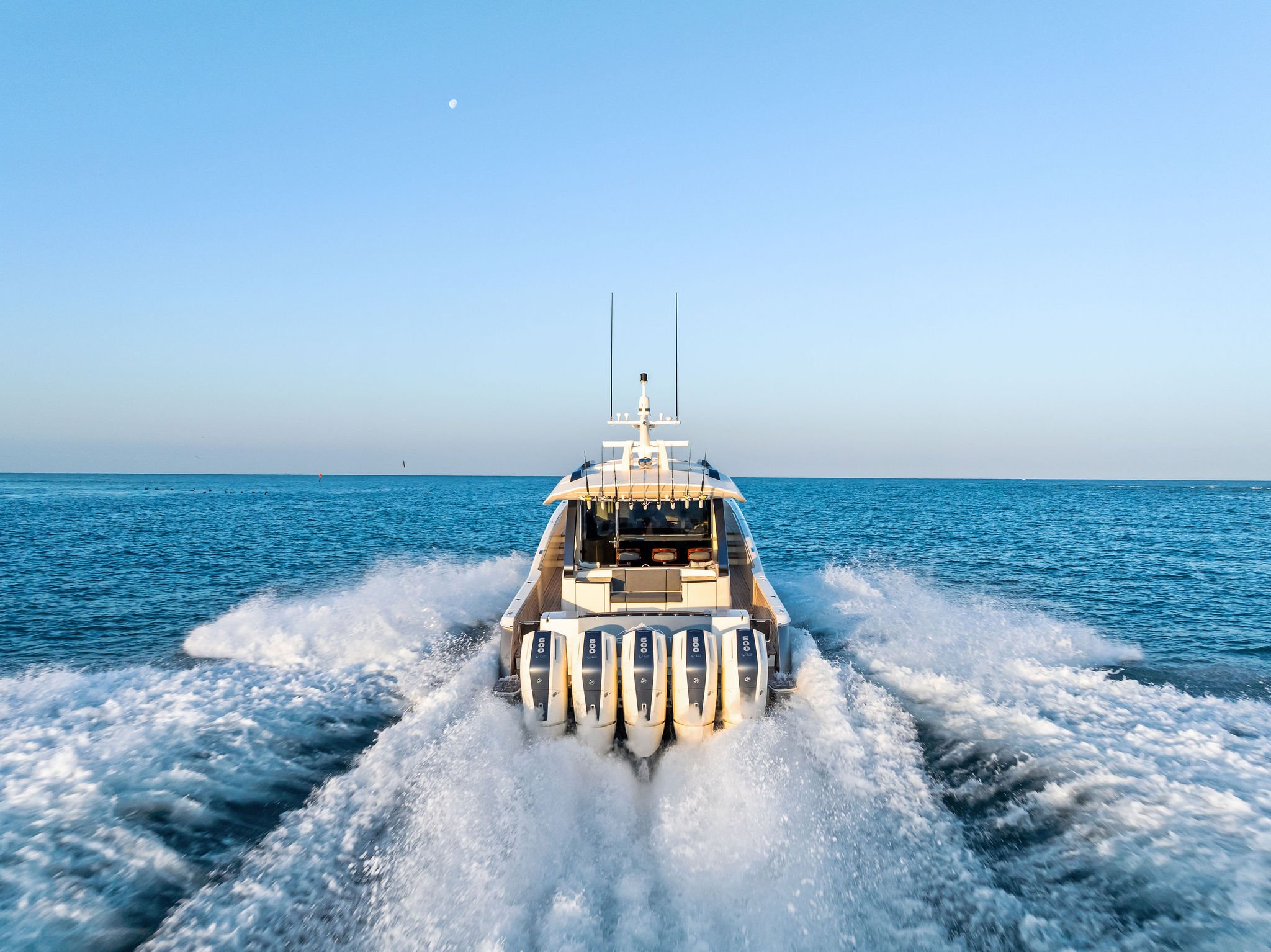 A yacht is traveling on open water, creating a wake behind it as it moves forward under a clear sky with a visible moon.