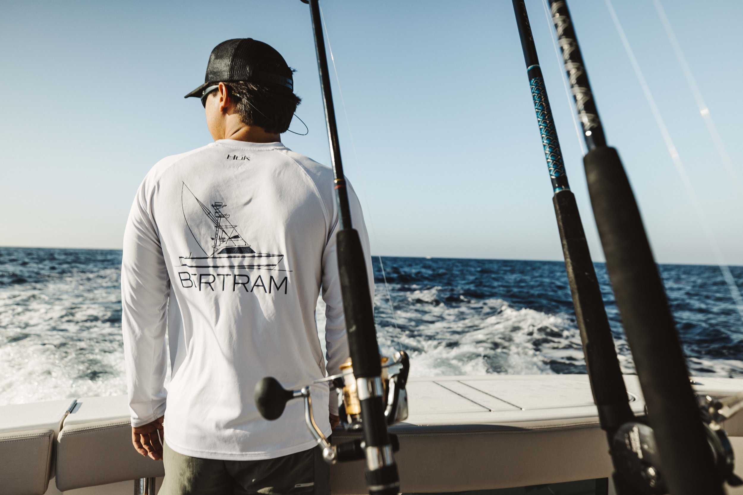 A man on a boat holding fishing rods with the ocean and sky in the background.