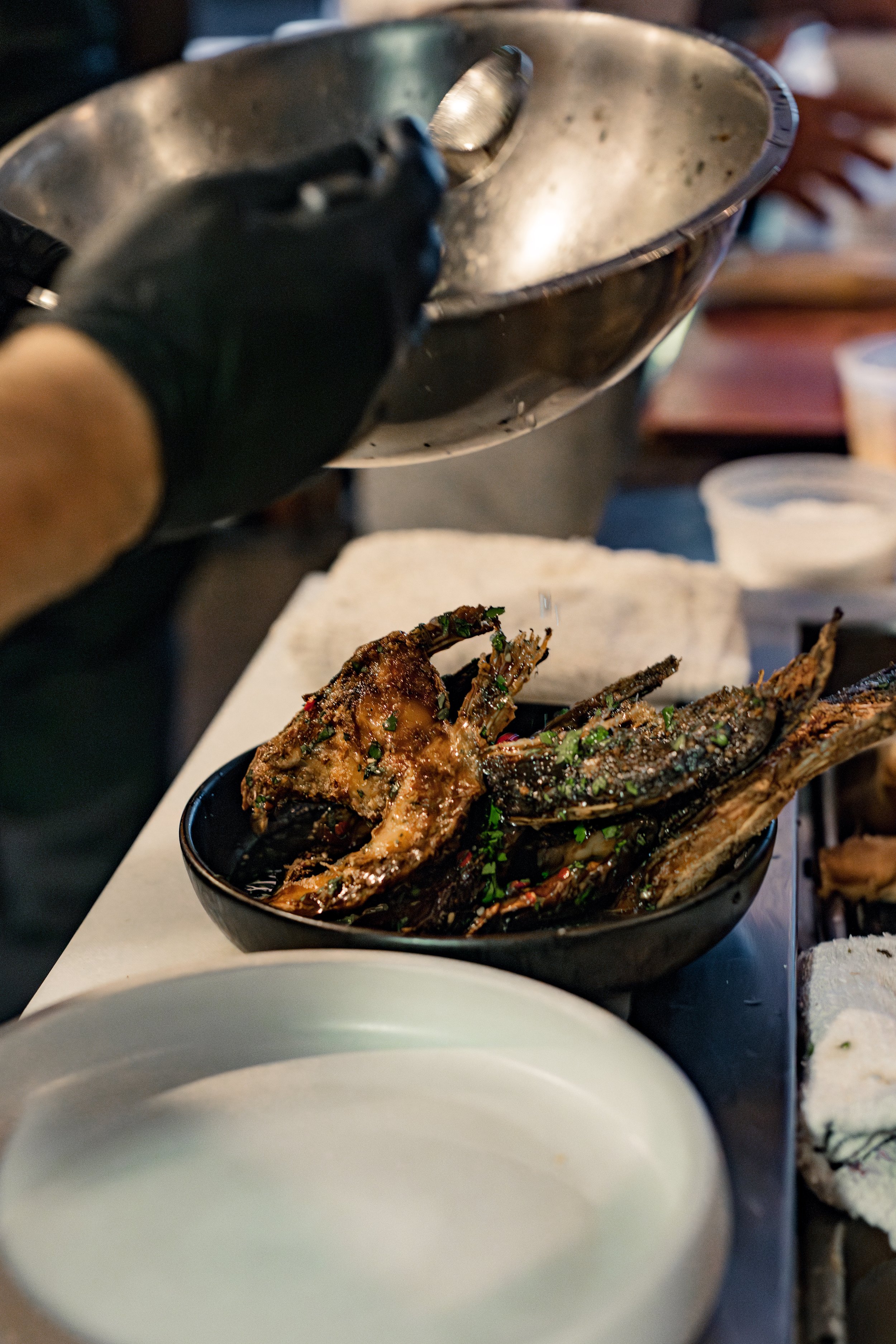 Someone pouring sauce over grilled fish in a black bowl.