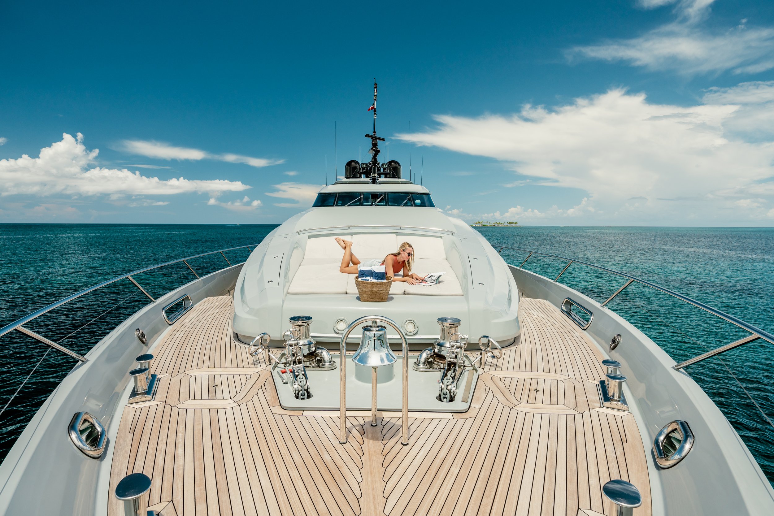 A woman relaxing on a yacht deck reading a magazine with ocean and blue sky in background.