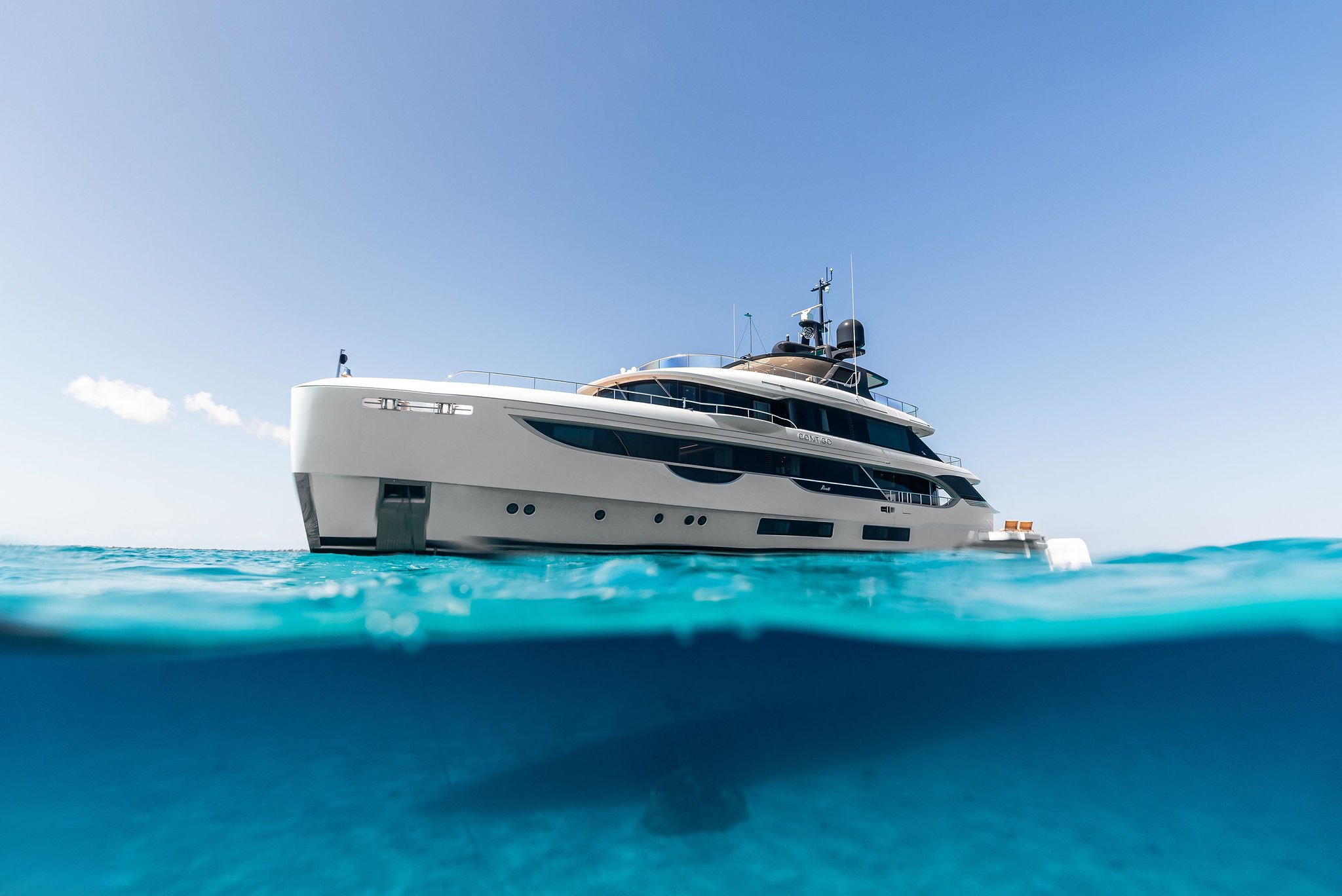 Modern white yacht floating on clear blue ocean under a bright blue sky.