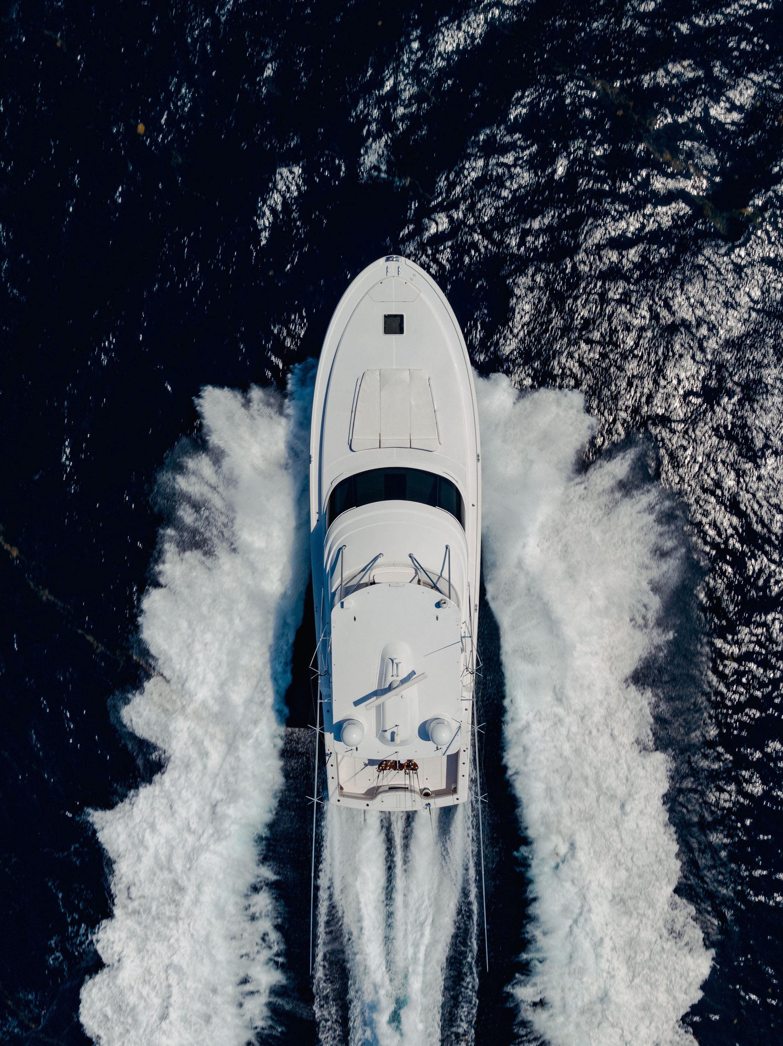 Aerial view of a white yacht speeding through deep blue ocean water, creating white waves and wake behind it.