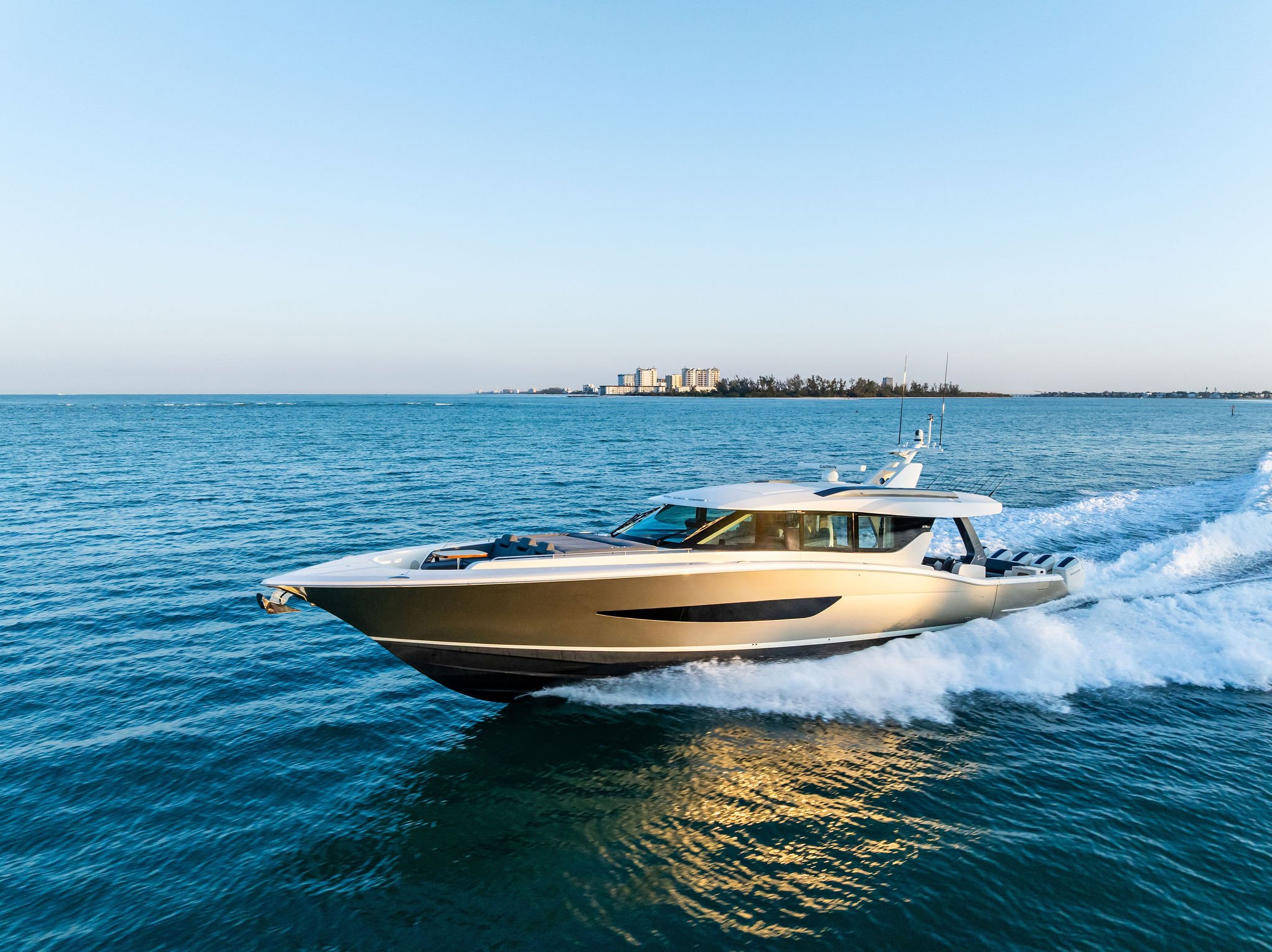 A luxury motorboat speeding through the water near a coastline with buildings and trees in the background.