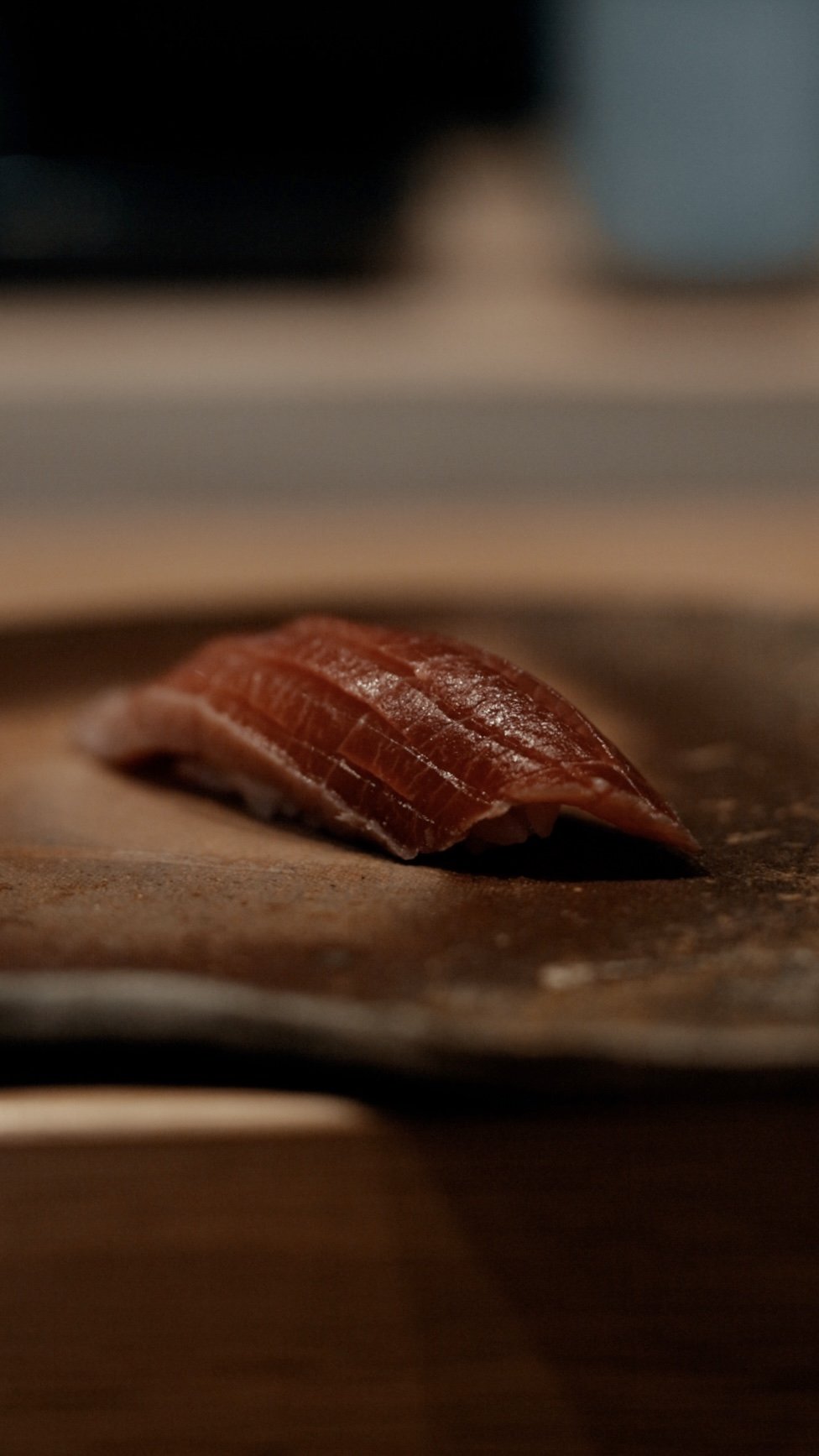 Close-up of a piece of sliced raw fish, likely tuna, resting on a wooden surface with a blurry background.