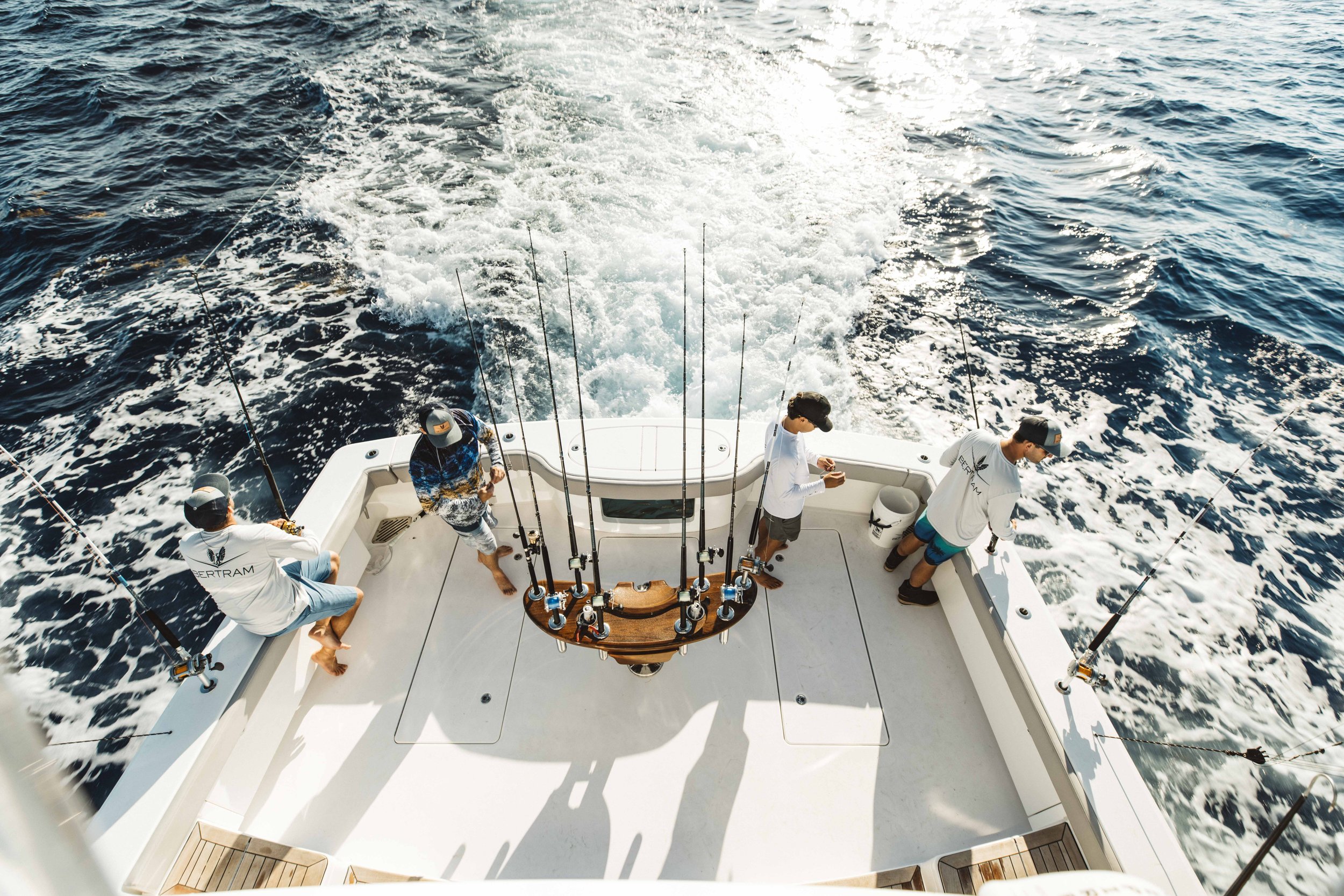 Four men stand on the deck of a boat, fishing with fishing rods in the ocean.