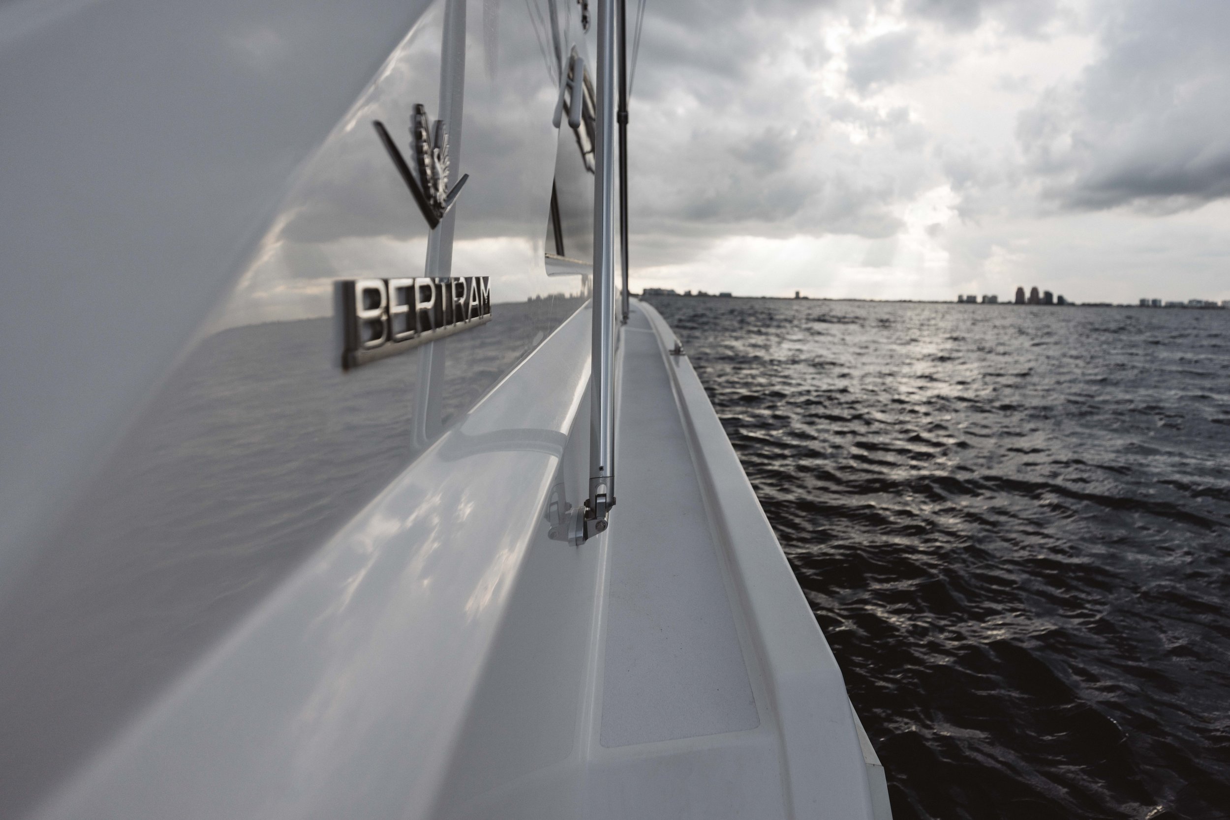 View from a boat showing a white hull with a Bertram logo, looking out over dark water and a cloudy sky.