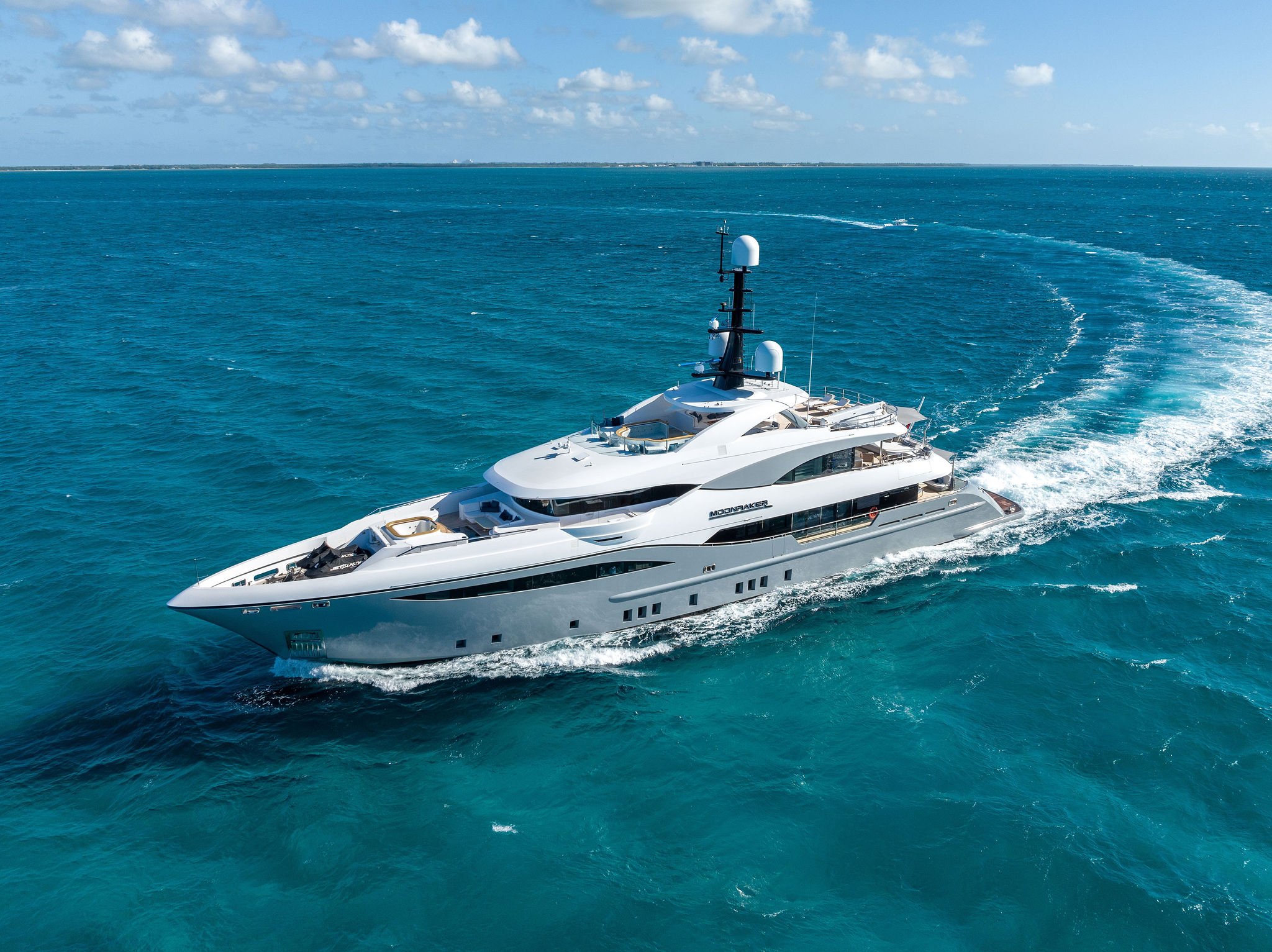 A luxurious white yacht sailing on clear blue ocean water under a partly cloudy sky.