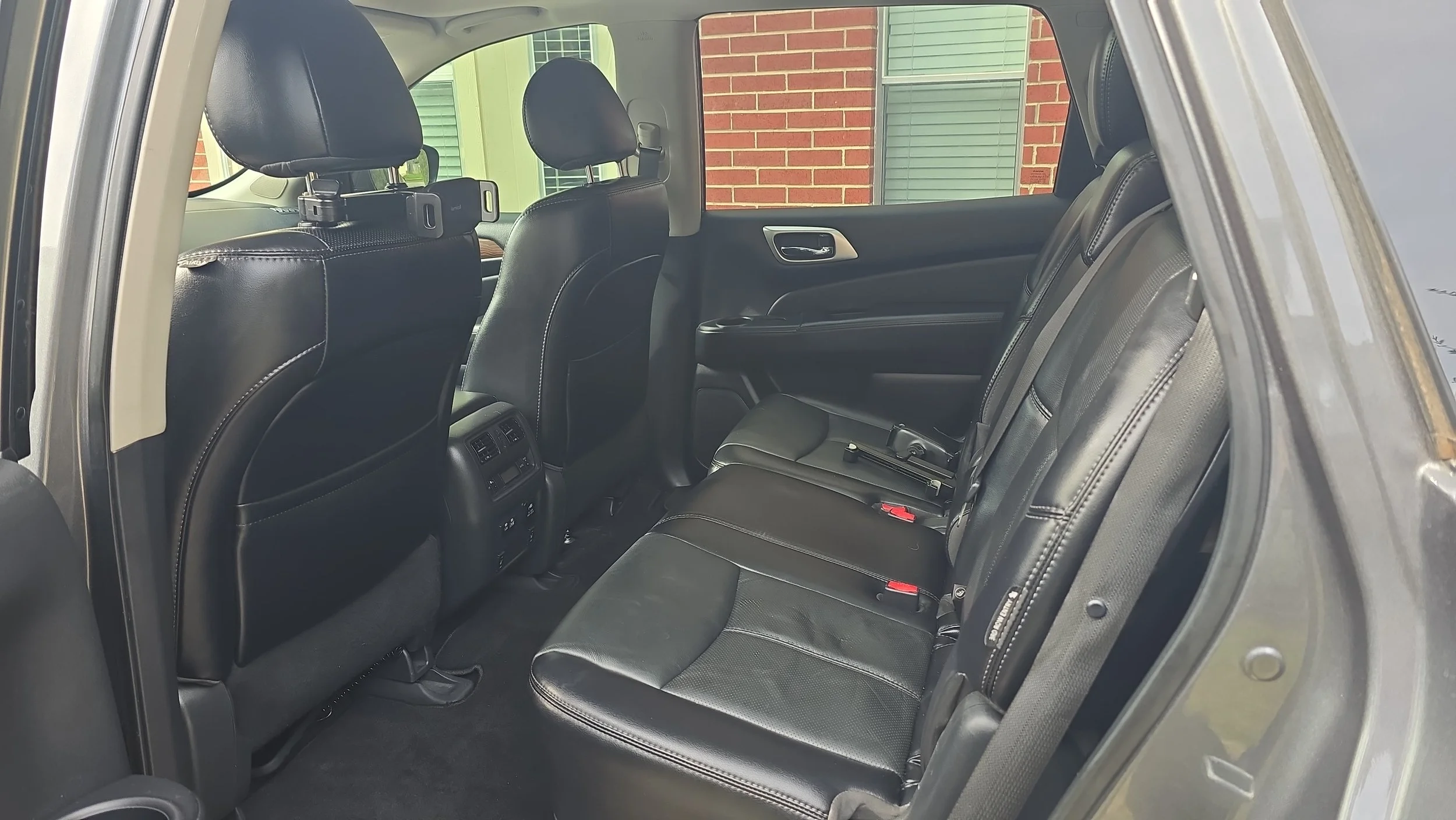 The interior of a black vehicle showing the back seat area with black leather seats, headrests, and rear vents, with a building with brick and siding visible through the windows.
