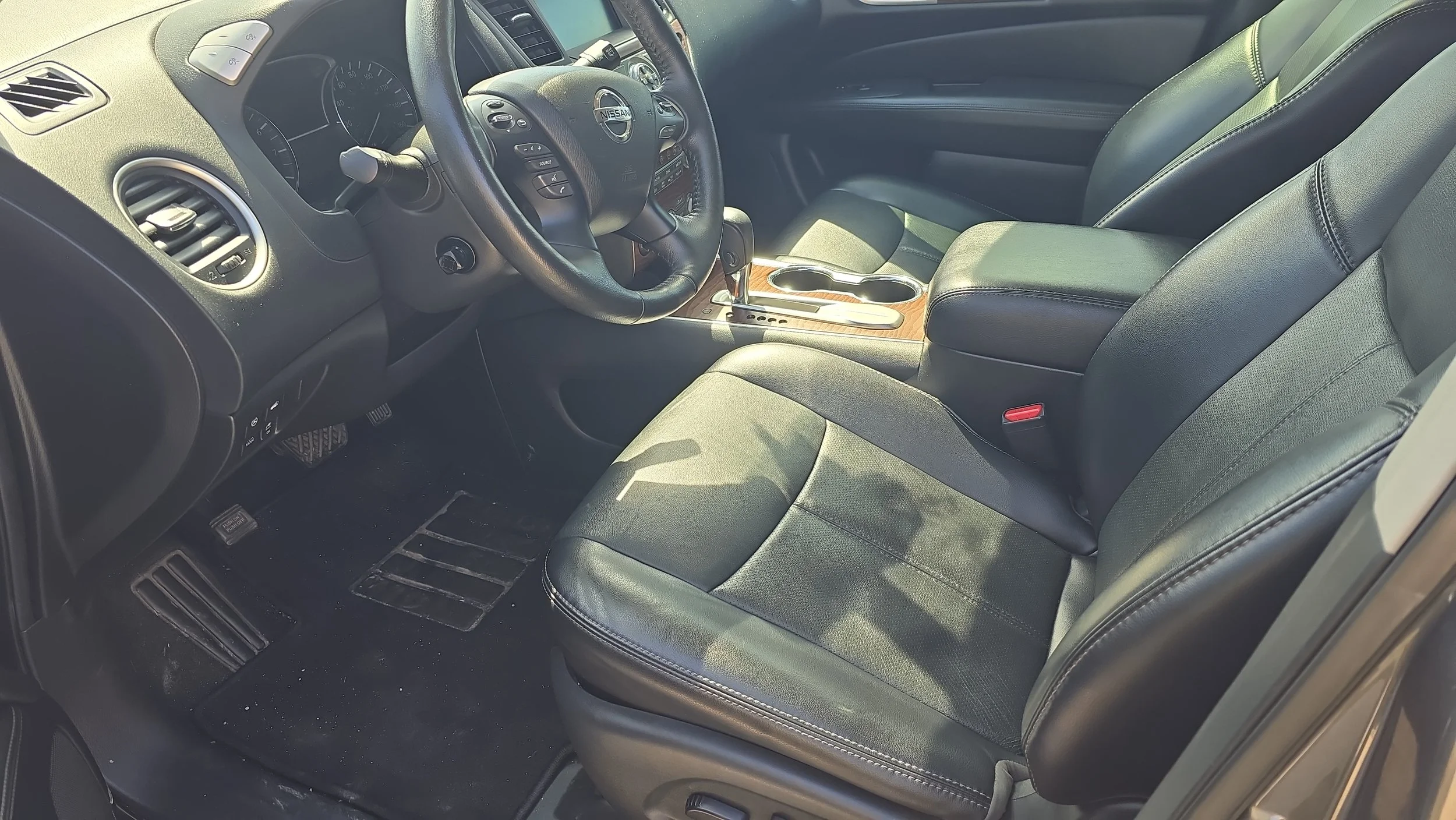Interior of a Nissan vehicle showing the driver's seat, steering wheel, dashboard, and center console with cup holders.