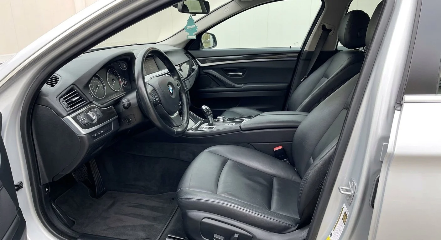 Interior of a BMW car showing the driver's seat, steering wheel, dashboard, and part of the passenger seat.