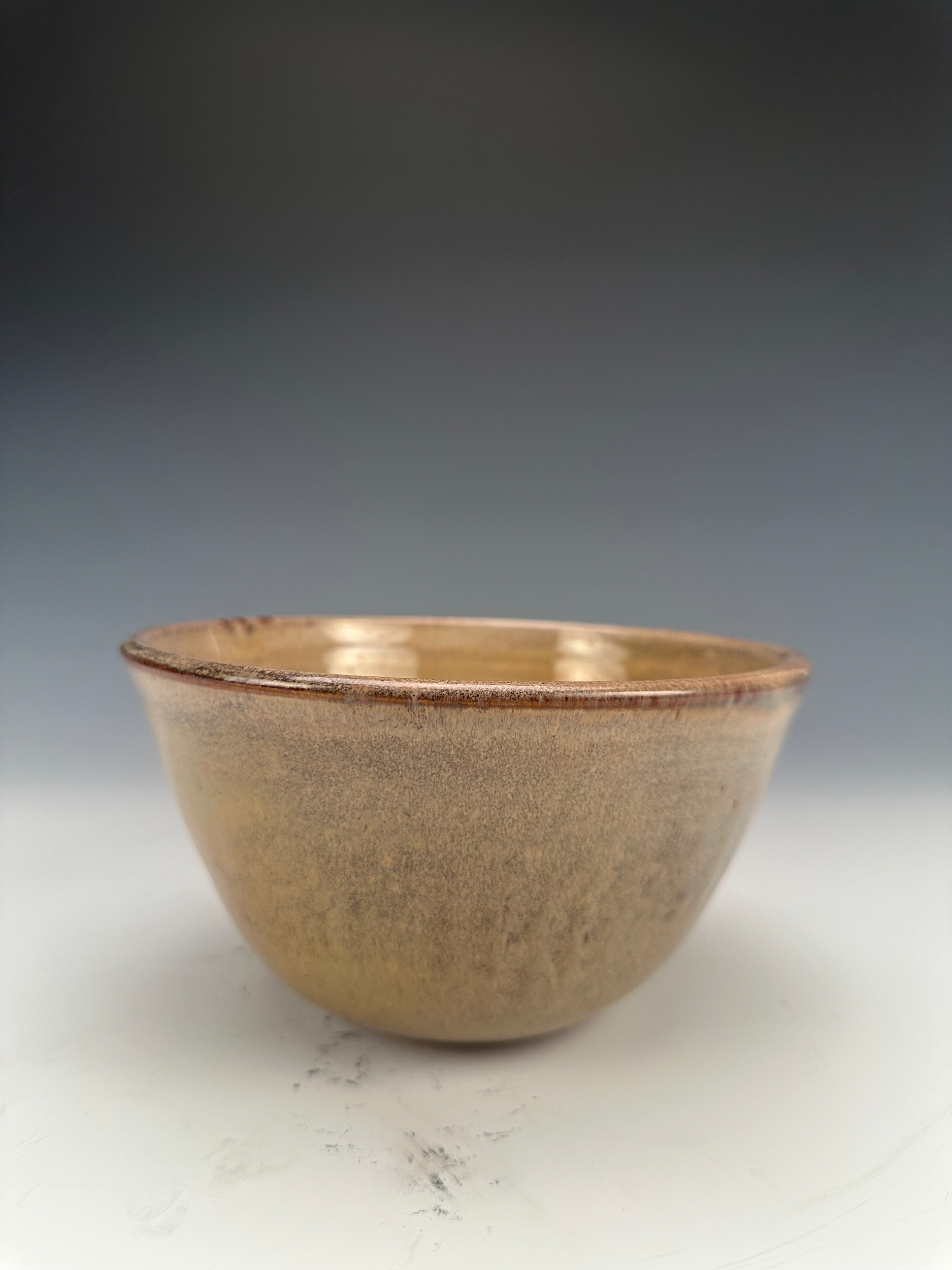 A close-up of a small beige ceramic bowl on a white surface with a gray background.