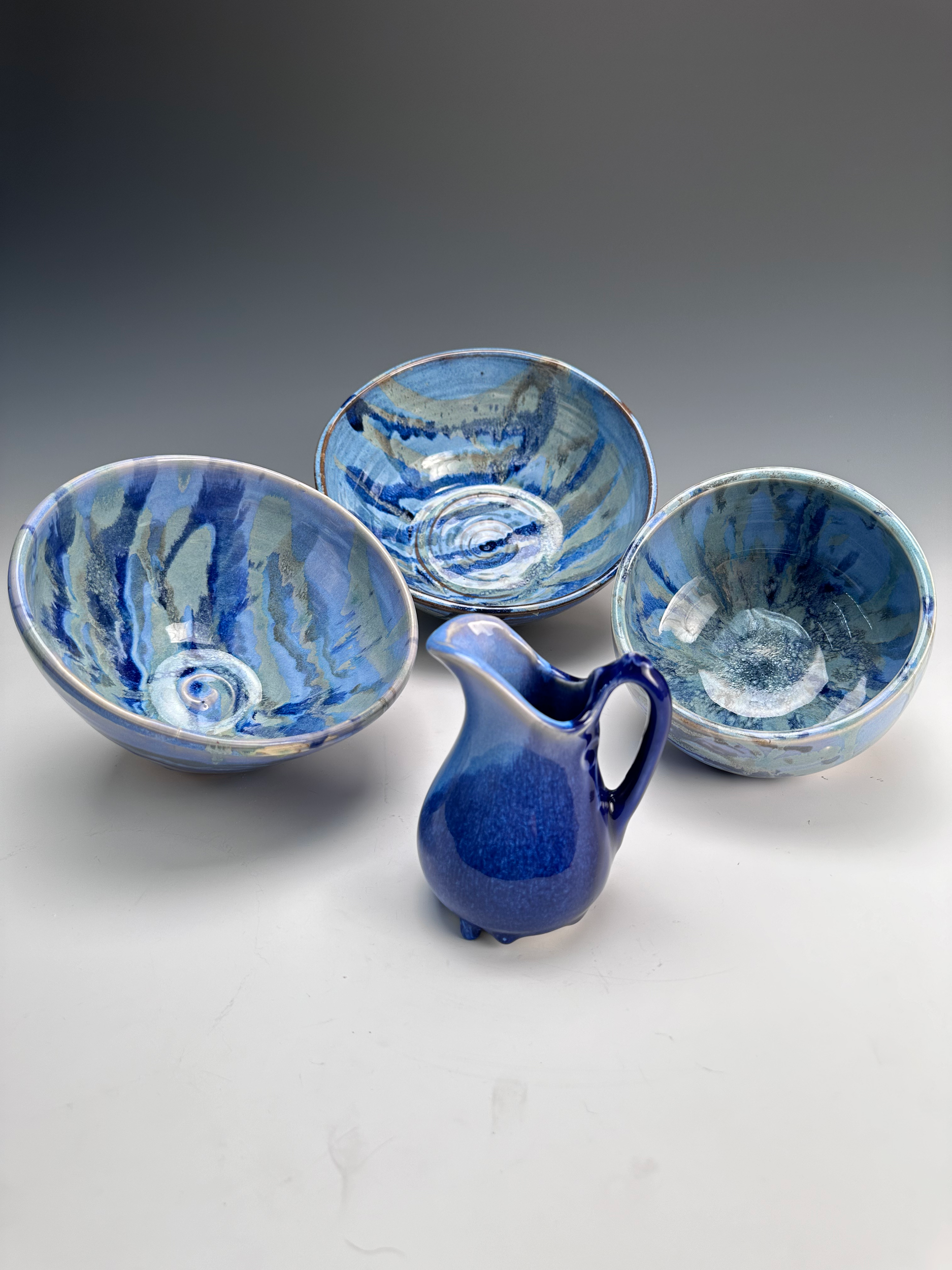 Blue ceramic pitcher and three blue glass bowls with swirling patterns on a white surface.