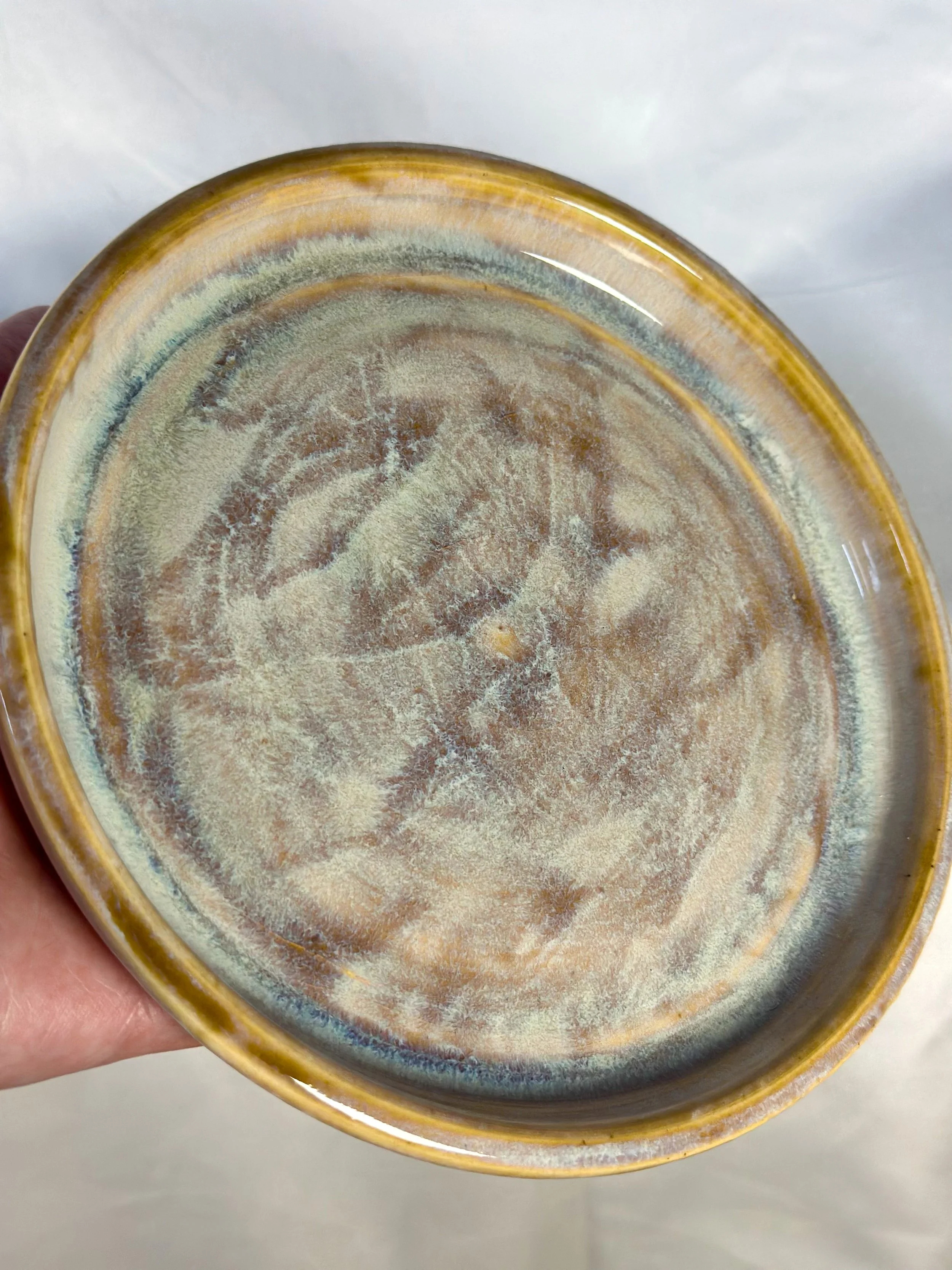 Close-up of the bottom of a ceramic bowl with a glazed, textured surface showing earthy colors and swirling patterns.