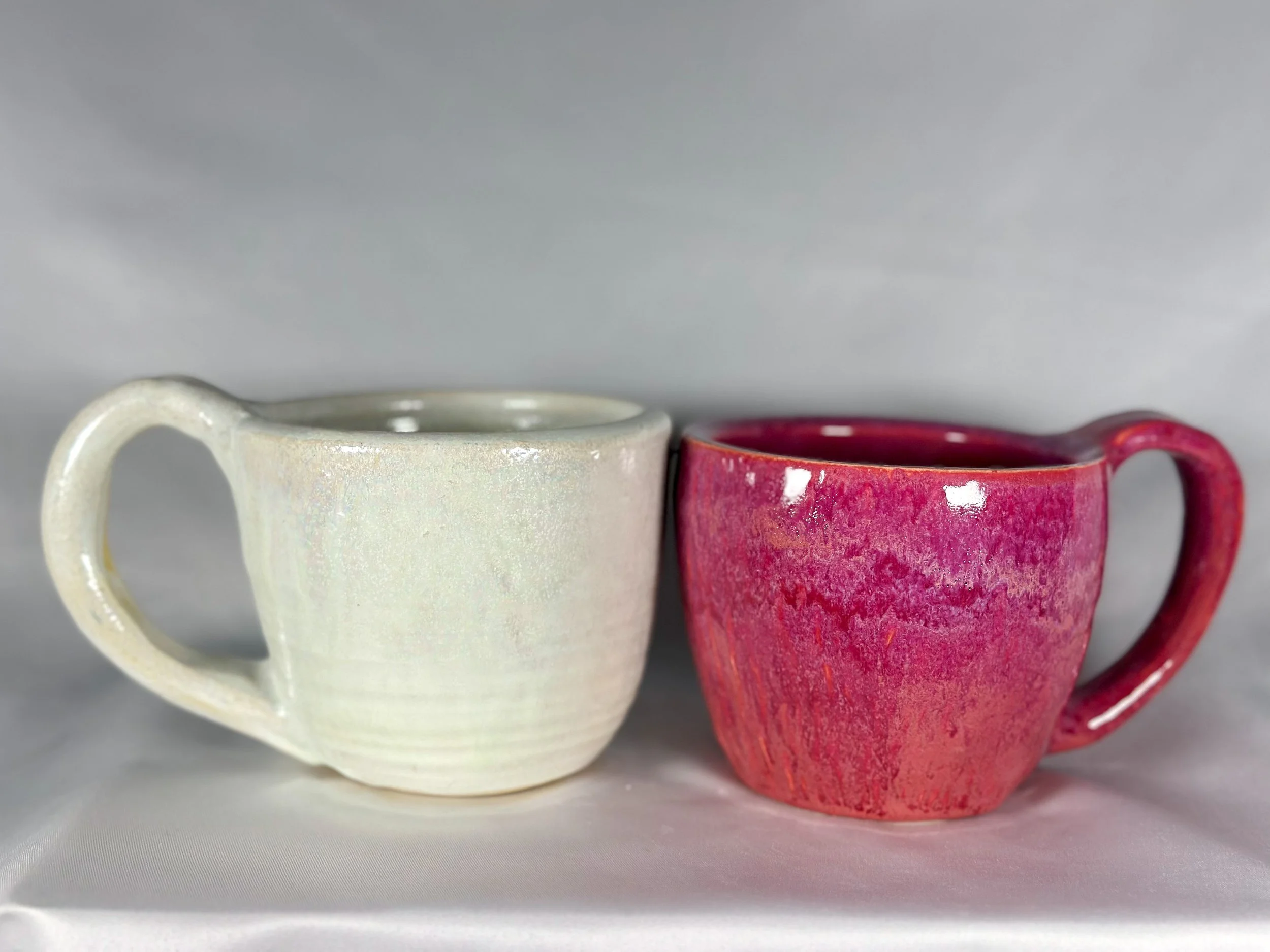 Two ceramic coffee mugs, one white and one pink, placed side by side on a white surface.