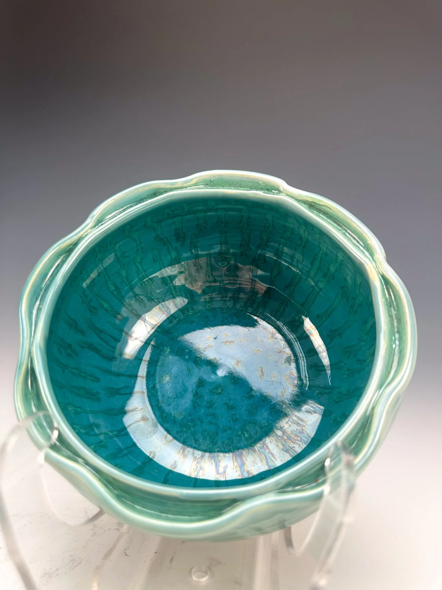 Inside view of a decorative glass bowl with green and blue hues, and wavy rim, placed on a clear stand