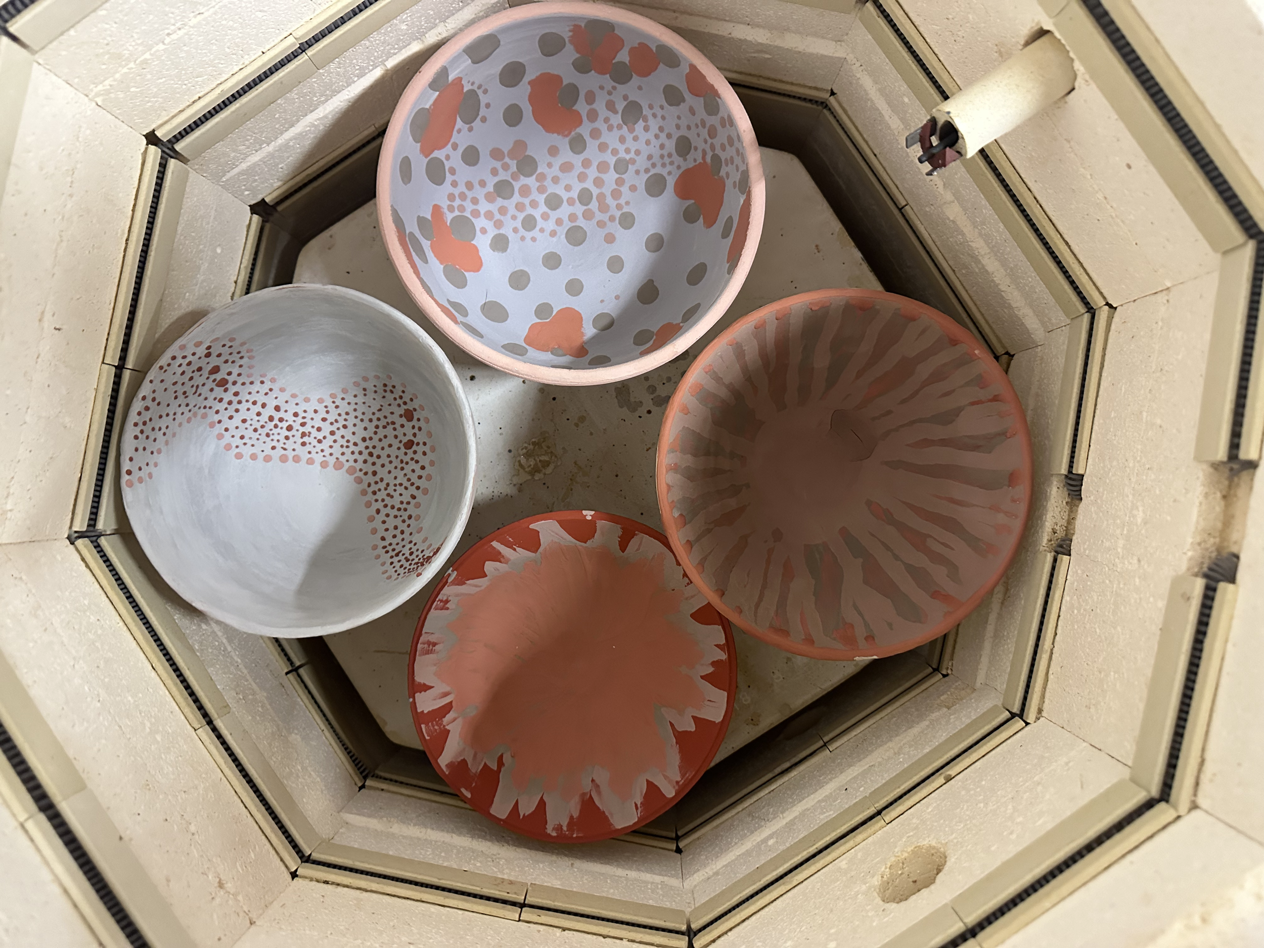 Four decorative bowls with abstract patterns seen from above inside a wood fireplace.