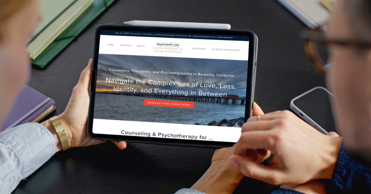 Two people looking at a tablet screen displaying a counseling website with a sunset over water in the background.