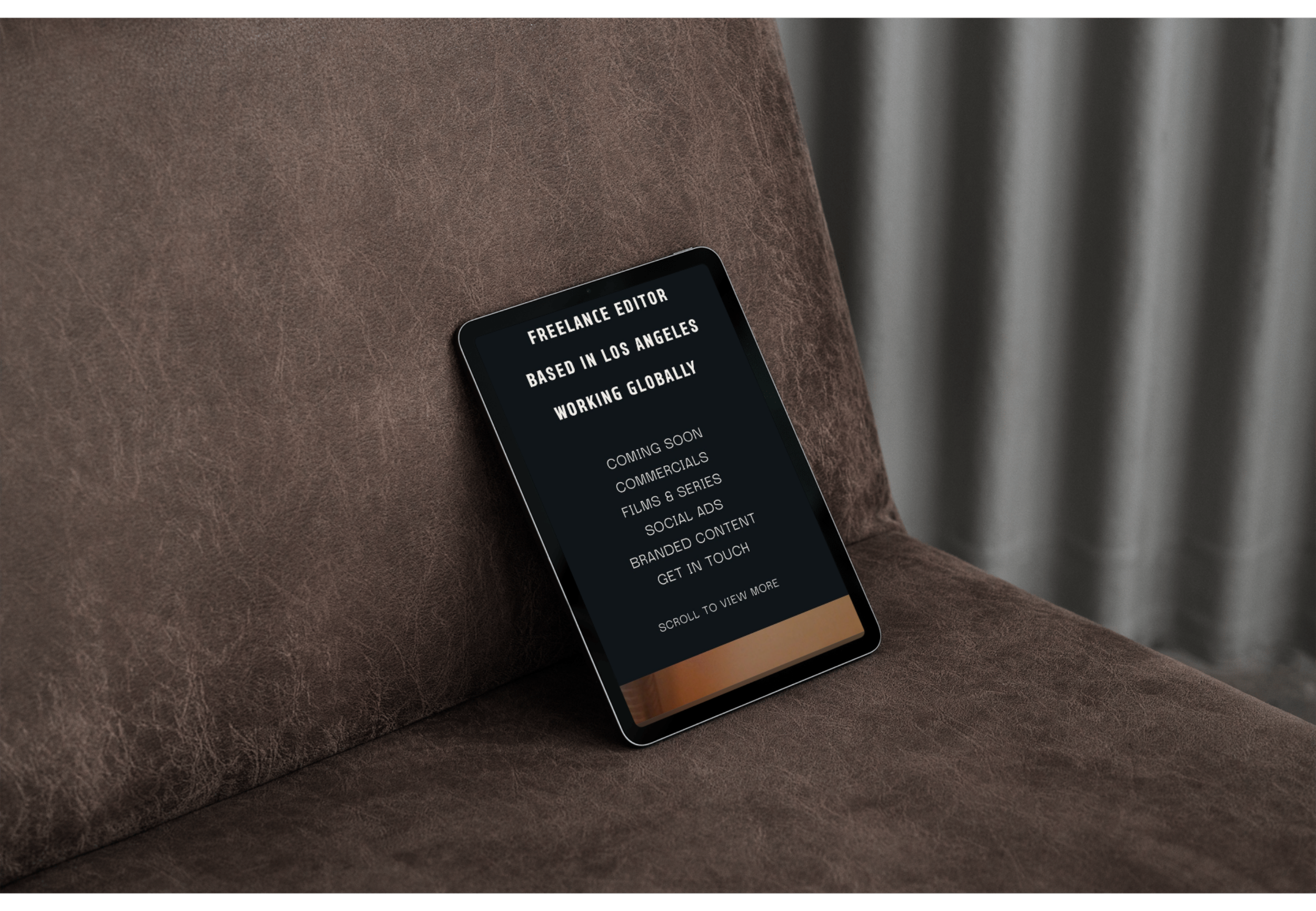 A smartphone resting on a brown leather couch displaying a black screen with white text about a freelance editor based in Los Angeles.