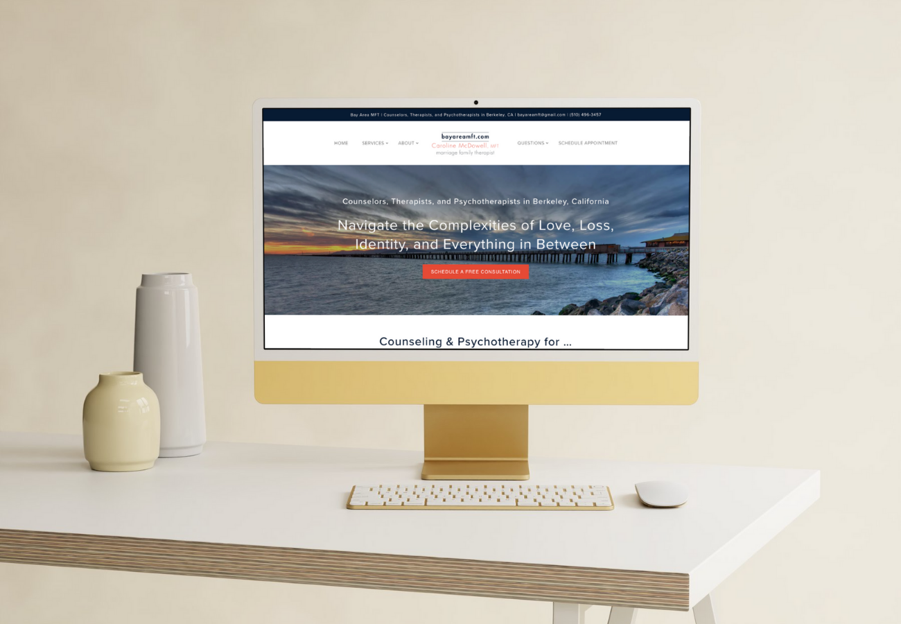 Computer screen displaying a counseling website with a scenic ocean view, on a white desk with vases, a keyboard, and a mouse.