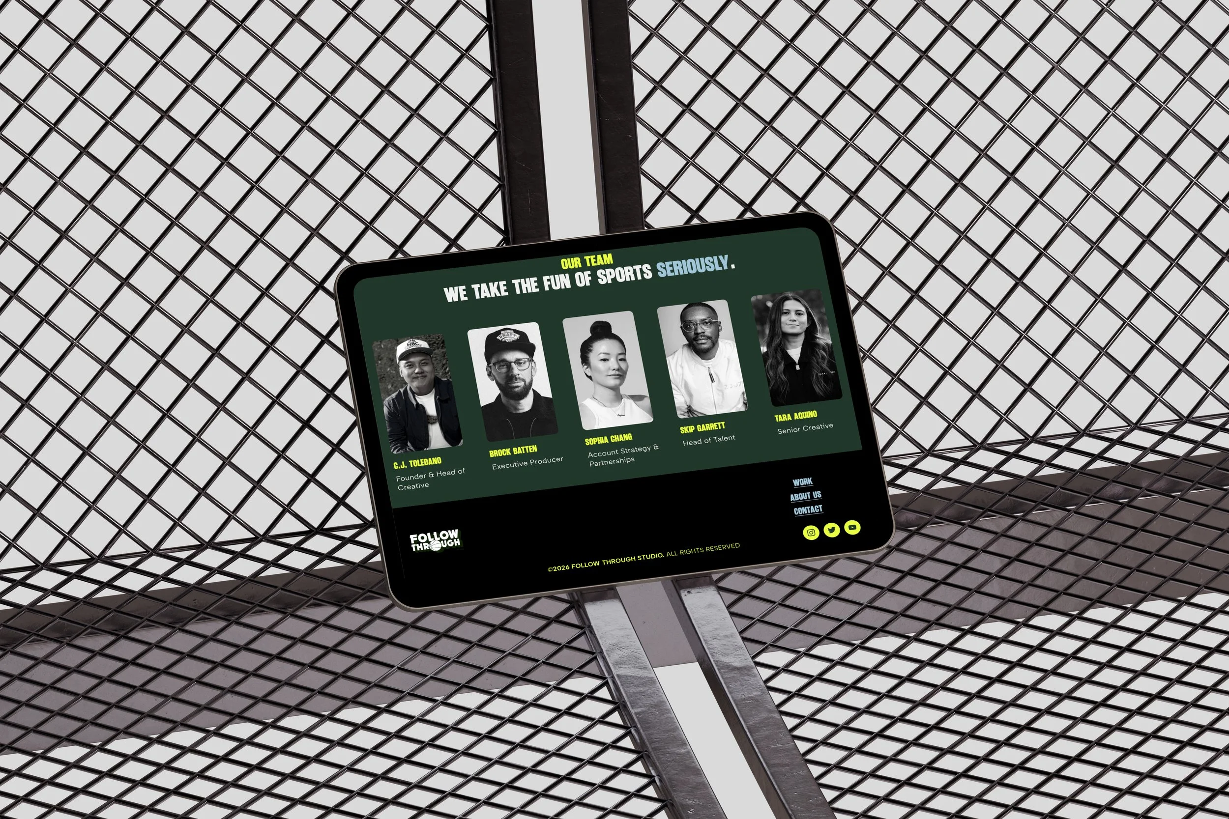 A computer screen on a metallic grid table displaying a website about a sports team, with photos of five team members and their titles.