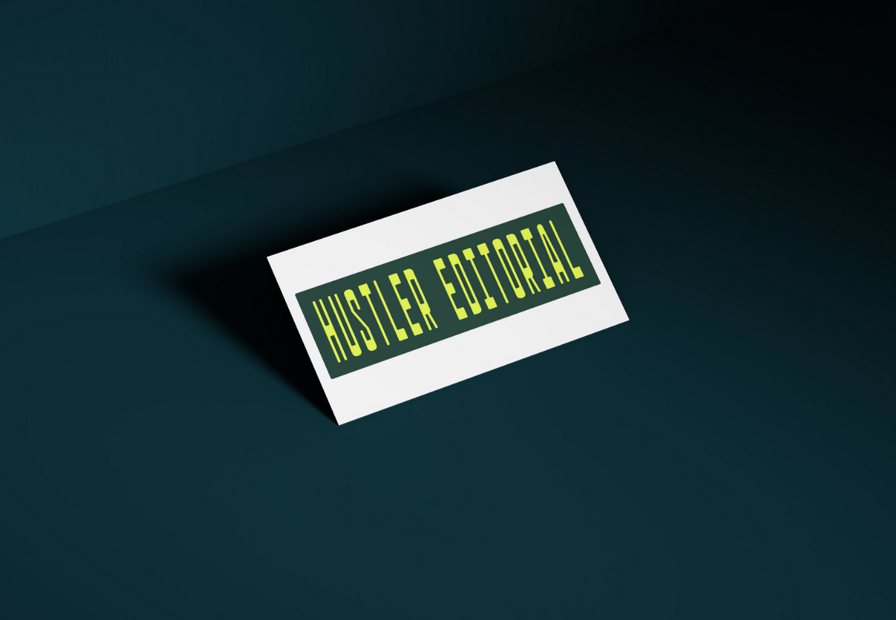 A white sign with green text reading 'HUSTLER EDITORIAL' placed on a dark surface, casting a shadow to the left.