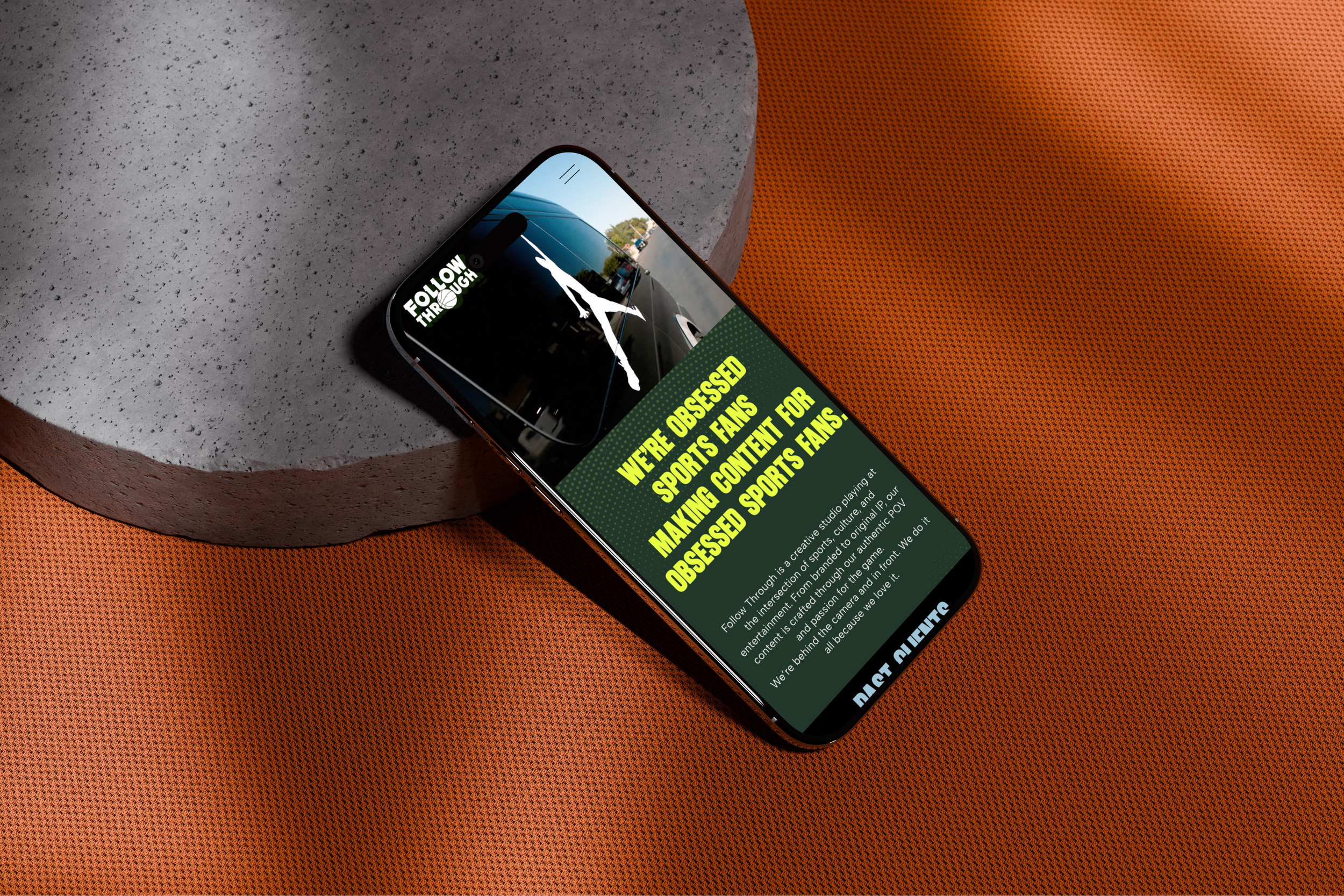 A smartphone lying on a textured orange surface displaying a website about sports fandom. The website includes a graphic of a person playing basketball and the text "Follow Through" and details about passionate sports fans.