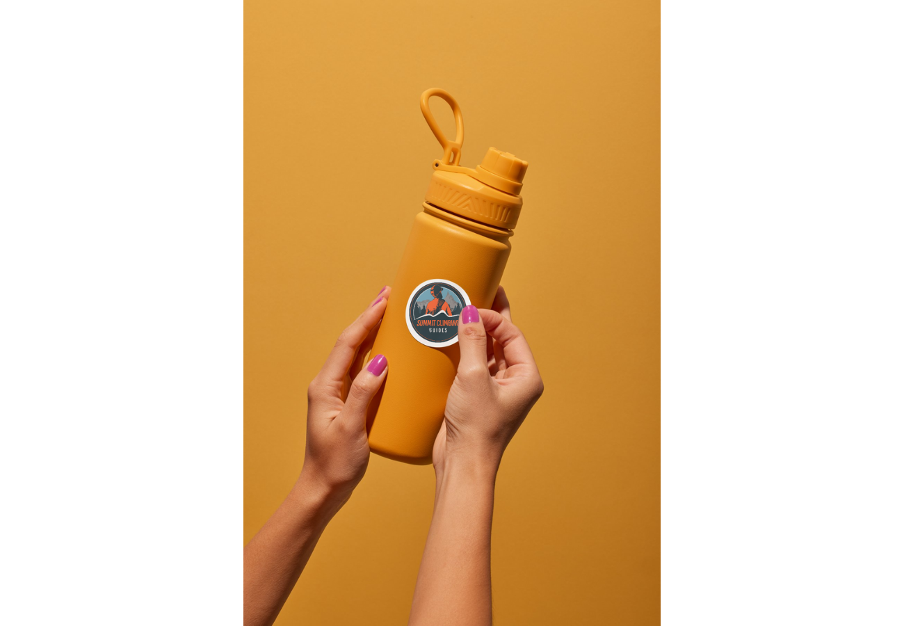 A person with pink nail polish holding a yellow water bottle with a sun visor sticker on it, against a yellow background.